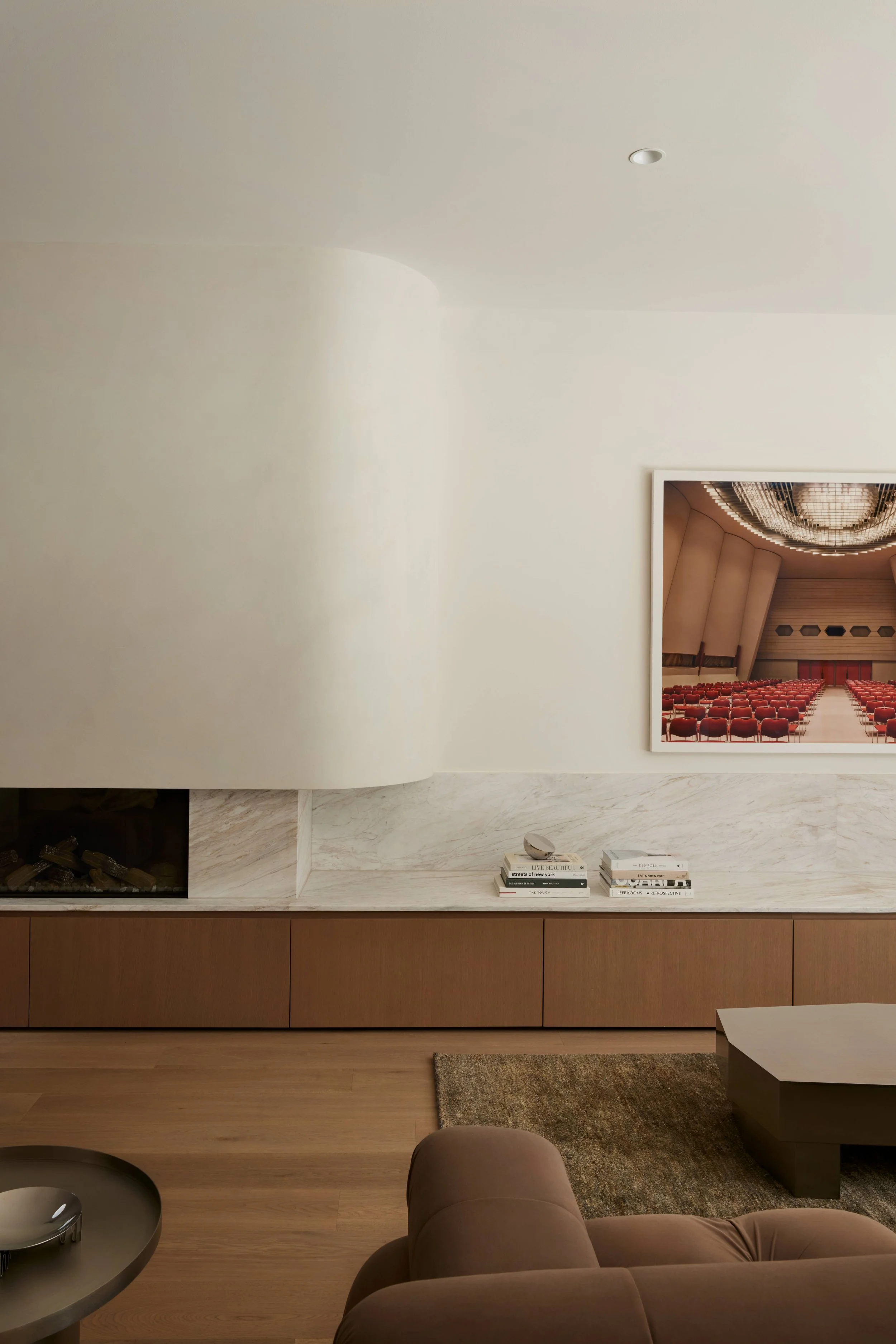 Modern living room with a cream-colored wall, a framed photo of an auditorium with red chairs, and a low wooden cabinet with books and a sculpture.