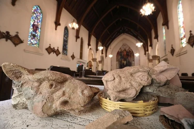  A pair of cast concrete gargoyle heads sits on a table at the back of the Nativity of the Blessed Virgin Mary church recently. The cast concrete details on the exterior of the church have been degrading recently due to chemical changes within the co