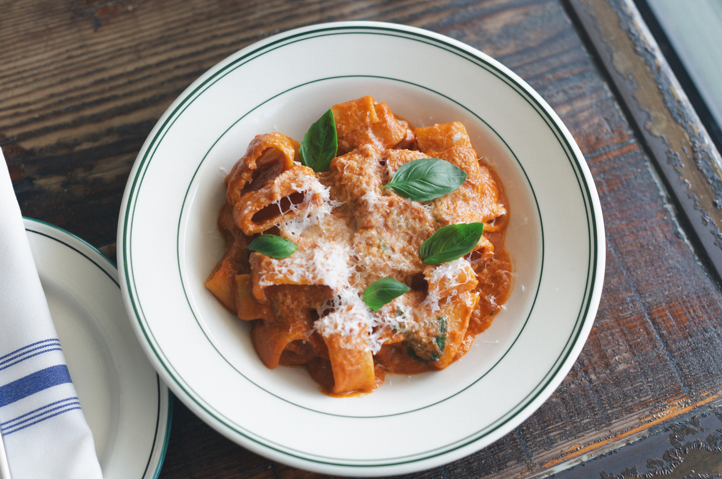 Plate of pasta with tomato sauce, topped with grated cheese and fresh basil leaves, on a wooden table.
