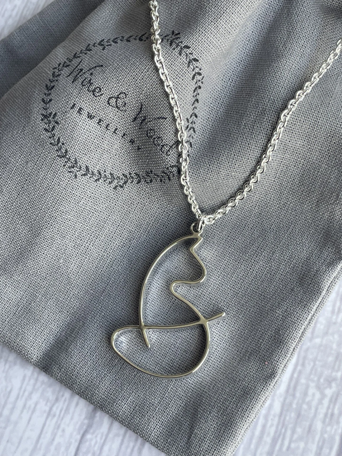 Silver necklace with a bird-shaped pendant resting on a grey fabric pouch.