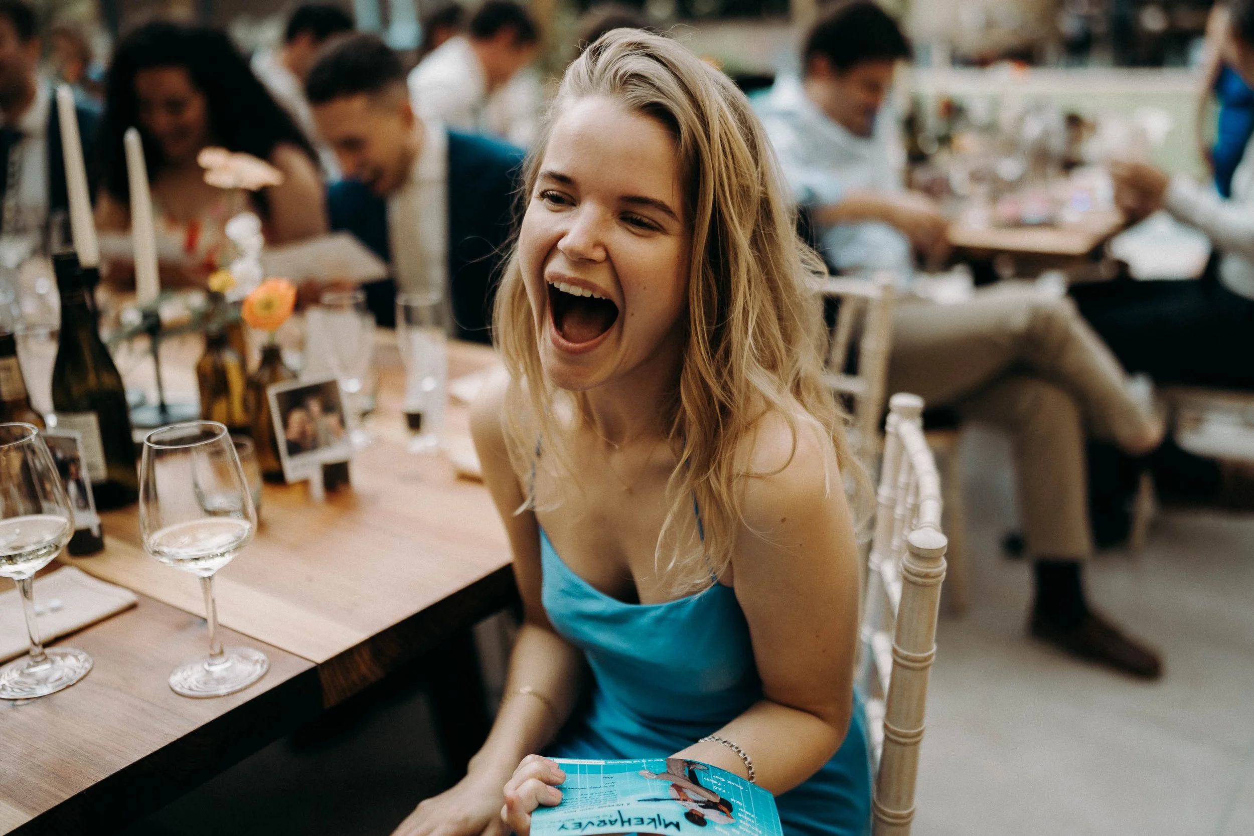 Wedding guest in a blue dress laughing at her table during the speeches at two woods estate