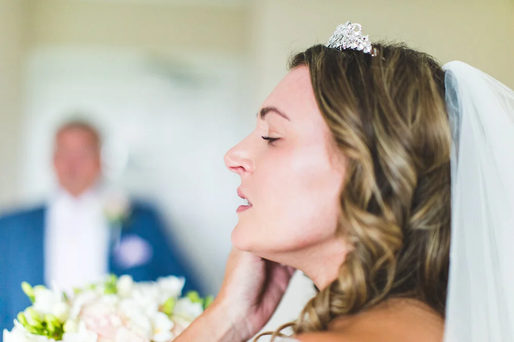 Bride in profile wearing a tiara and veil, holding a bouquet with a blurred background.