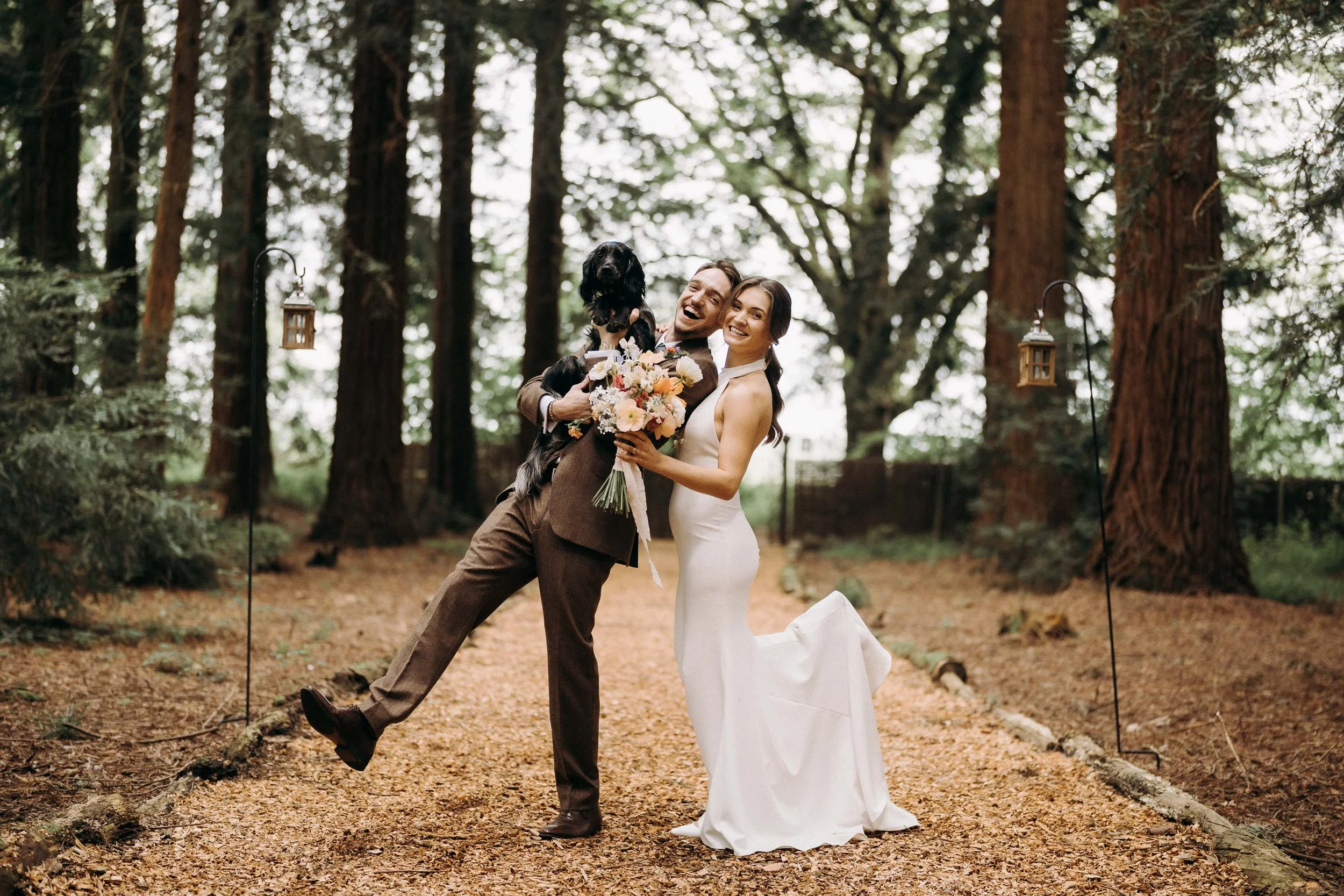 Bride and groom lifting their dog and laughing together in the forest at Two Woods Estate.