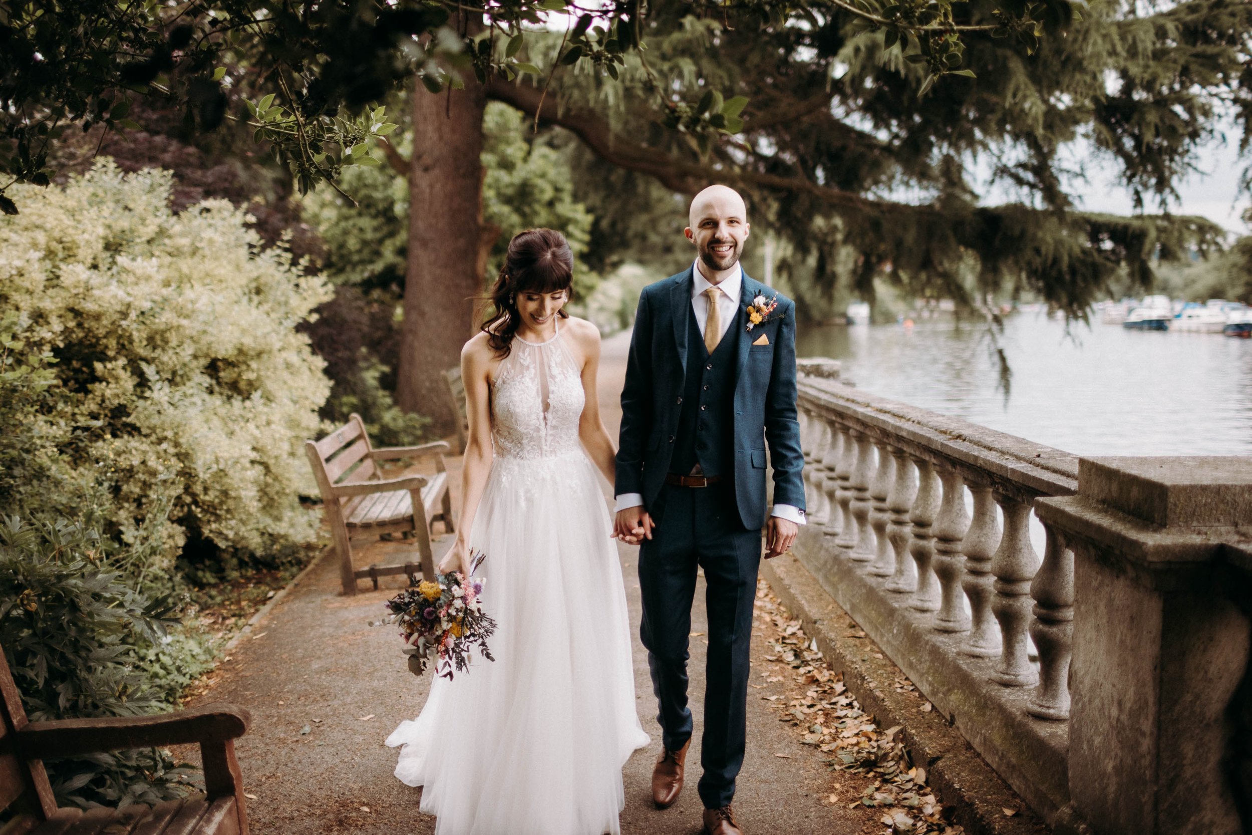 Bride and groom walking along a the thames surrounded by trees after their ceremony at Orleans House Gallery.