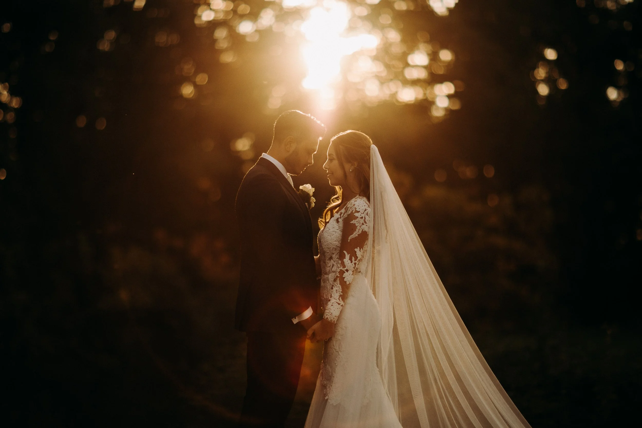 Bride and groom embracing at Kasteel Heeswijk, framed by soft sunset light and elegant lace details on the bride’s veil.