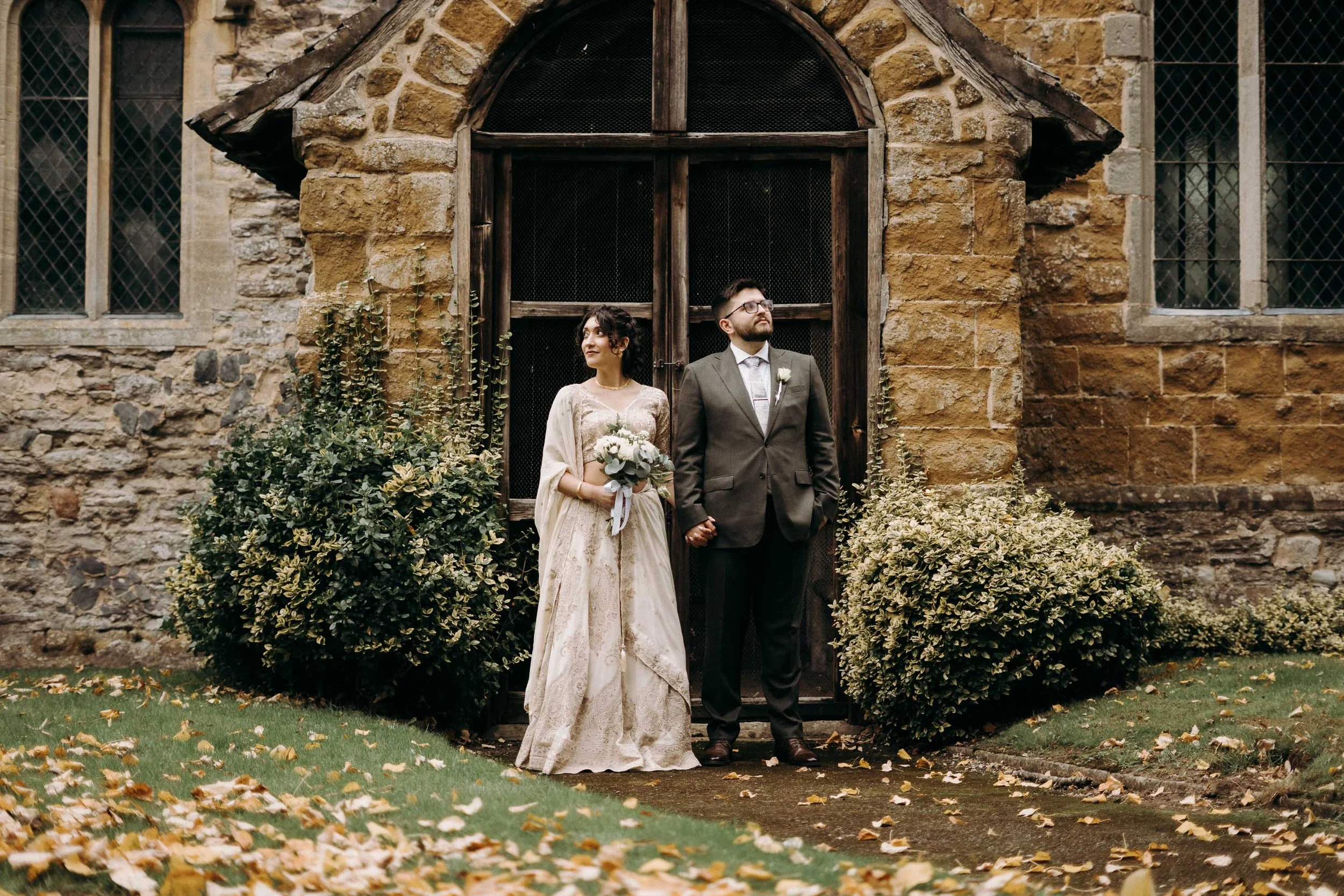 Bride and groom standing together outside a historic stone building at Brooksby Hall.