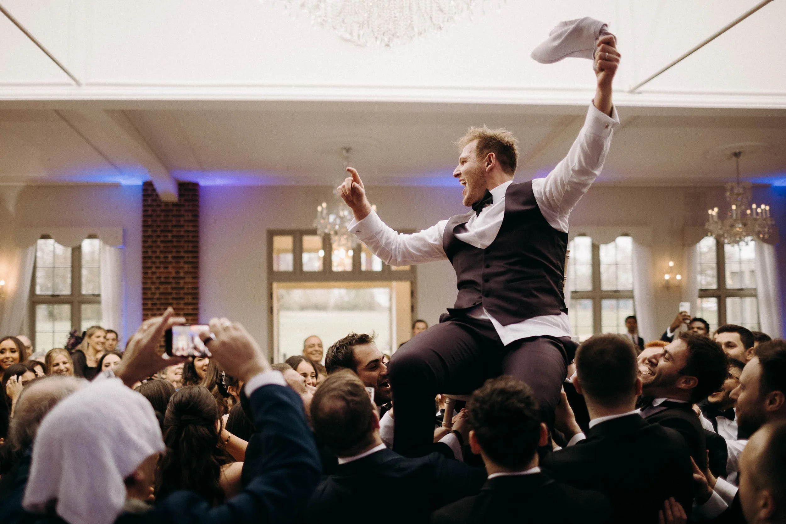 Jewish groom lifted above the wedding guests on a chair as he celebrates his marriage at Offley Place.
