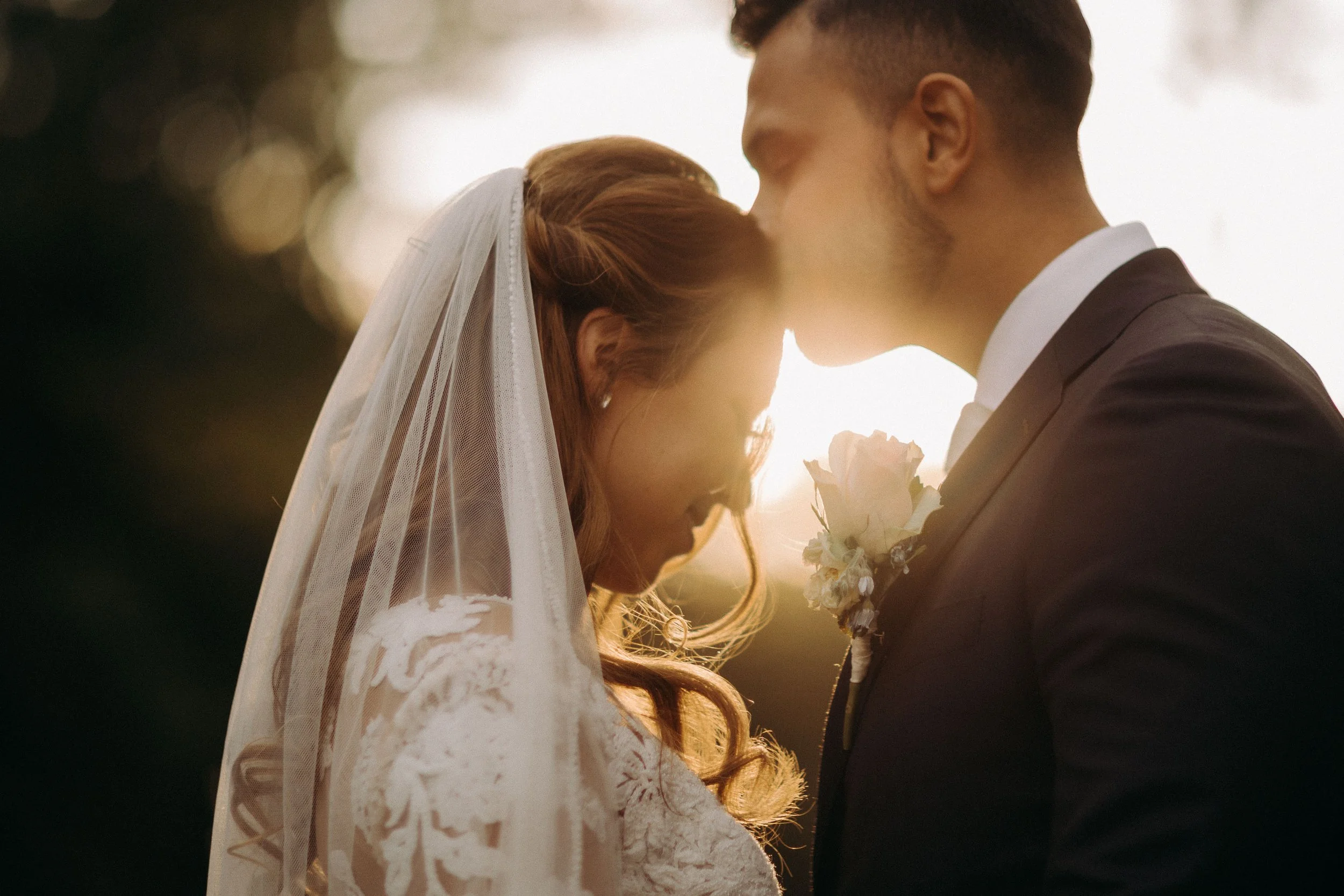 Groom kissing the bride’s forehead at Kasteel Heeswijk during sunset, with soft golden light illuminating her veil.