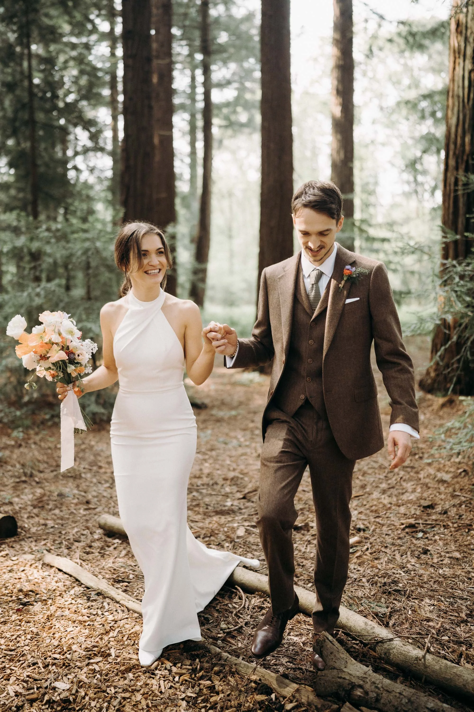 Bride and groom walking hand in hand through the woodland at Two Woods Estate.