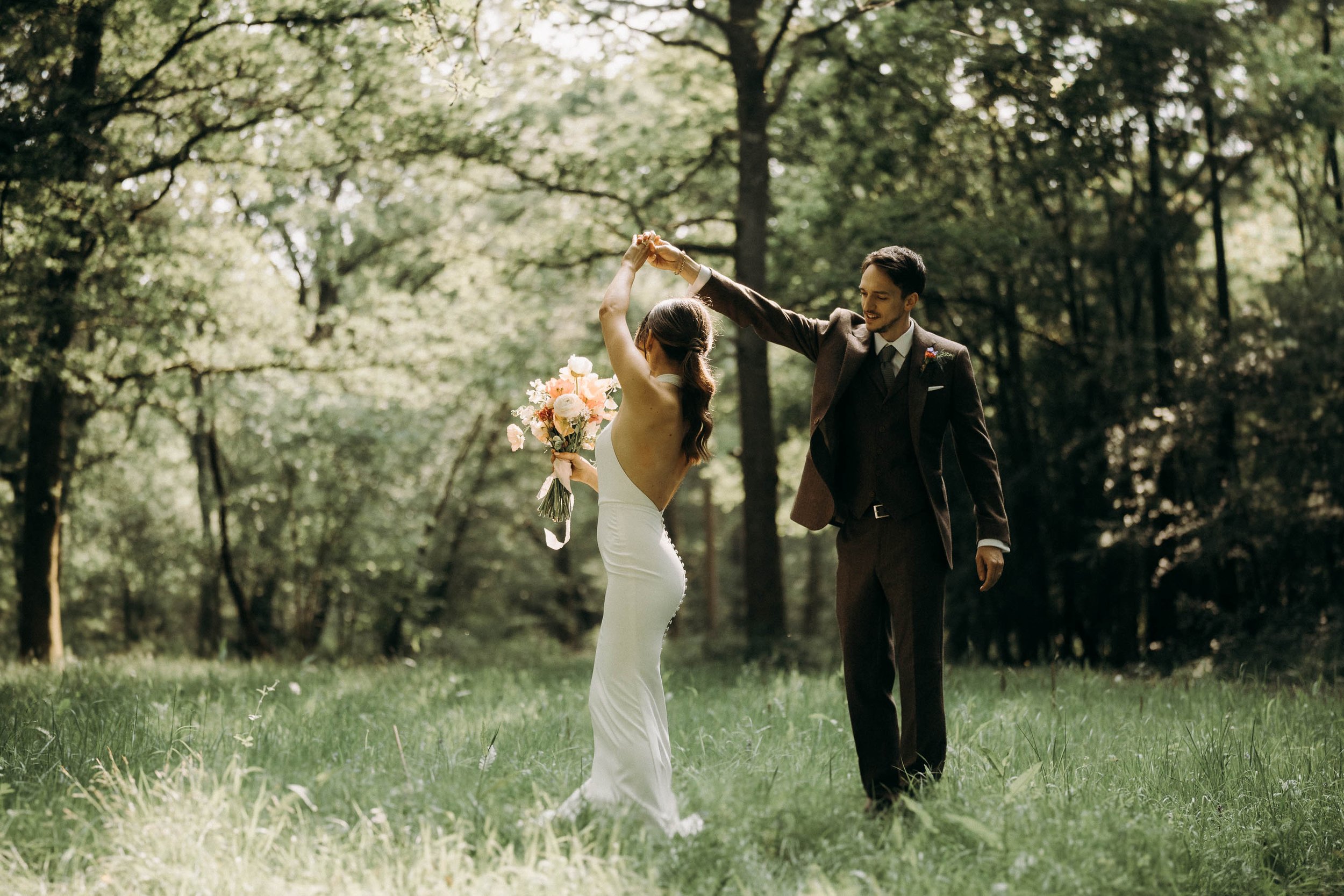 Bride and groom dancing in the forest clearing at Two Woods Estate, with sunlight filtering through the tall trees around them.
