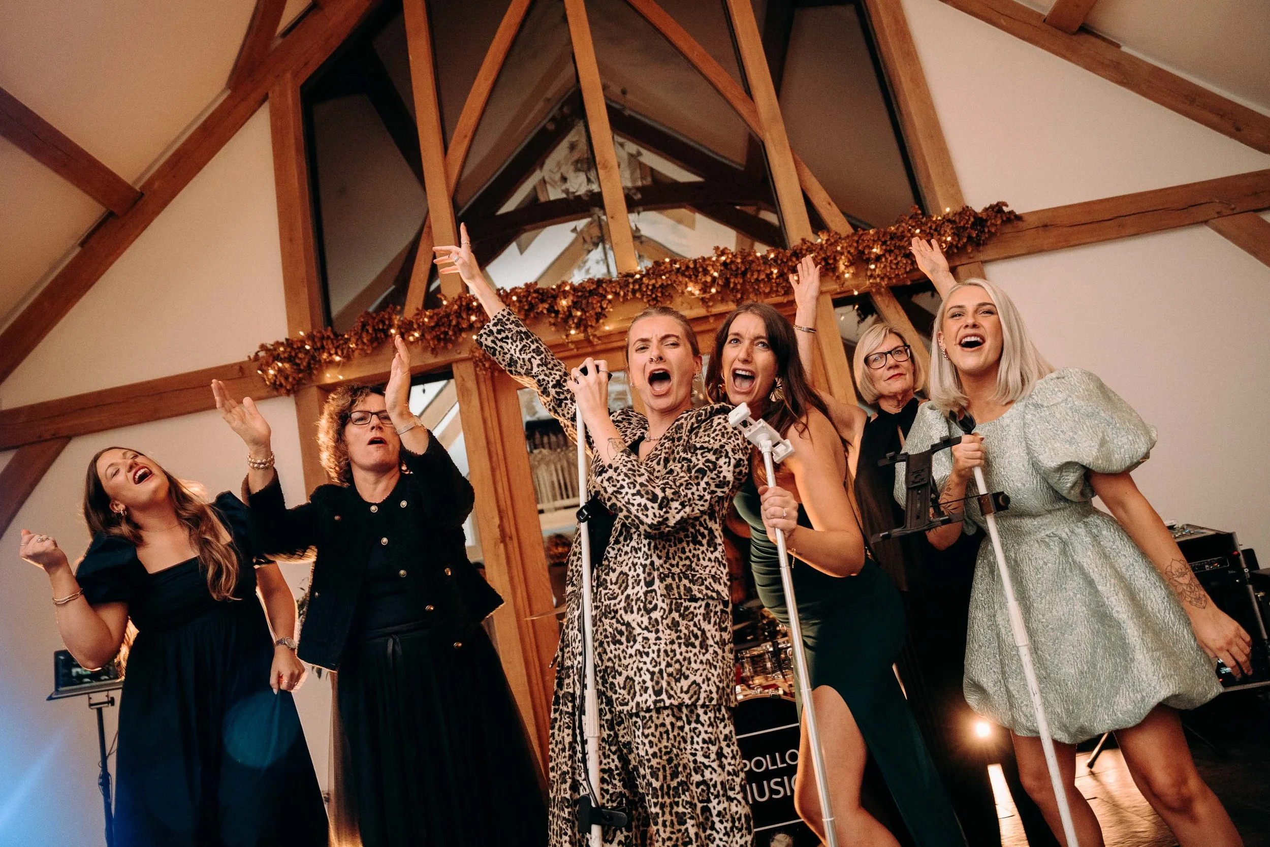 Female wedding guests sing with microphones during the wedding reception at Mythe Barn.