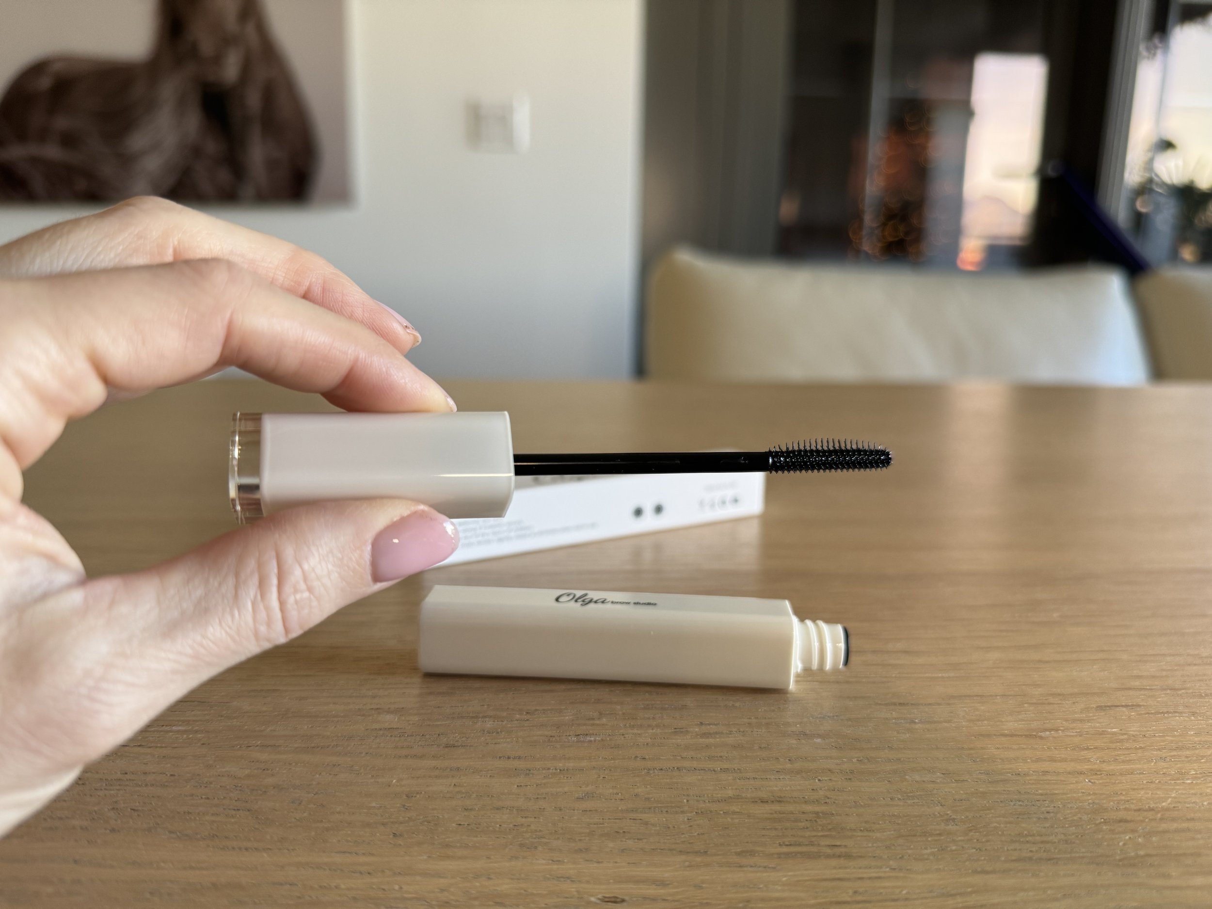 woman's hand holding best clean brow gel applicator in front of wooden table