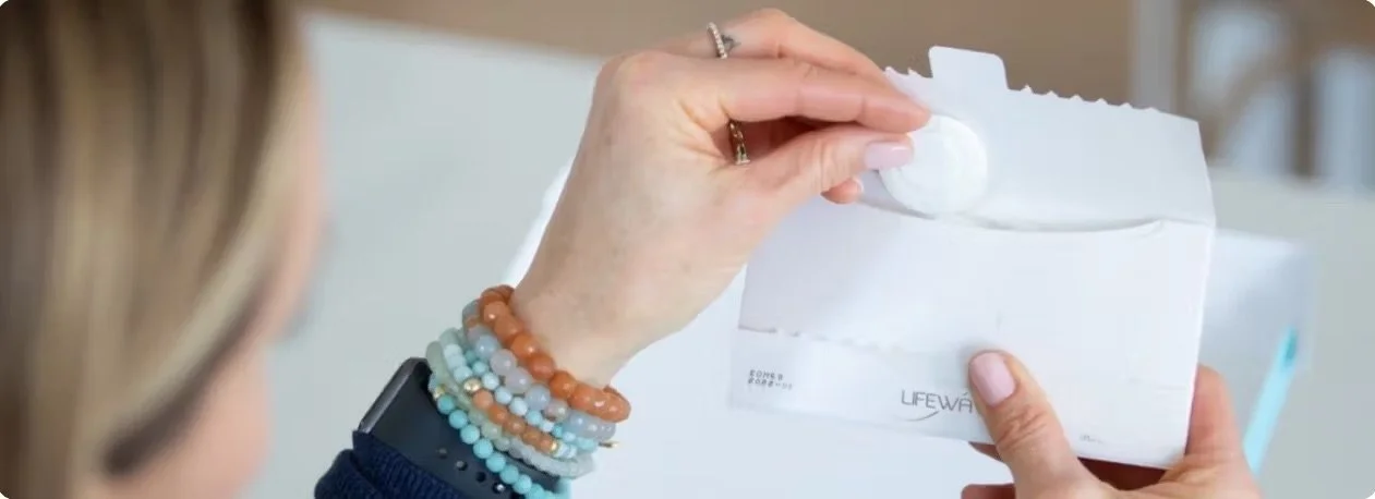 womans hand with bracelets holding a Lifewave patch and envelope