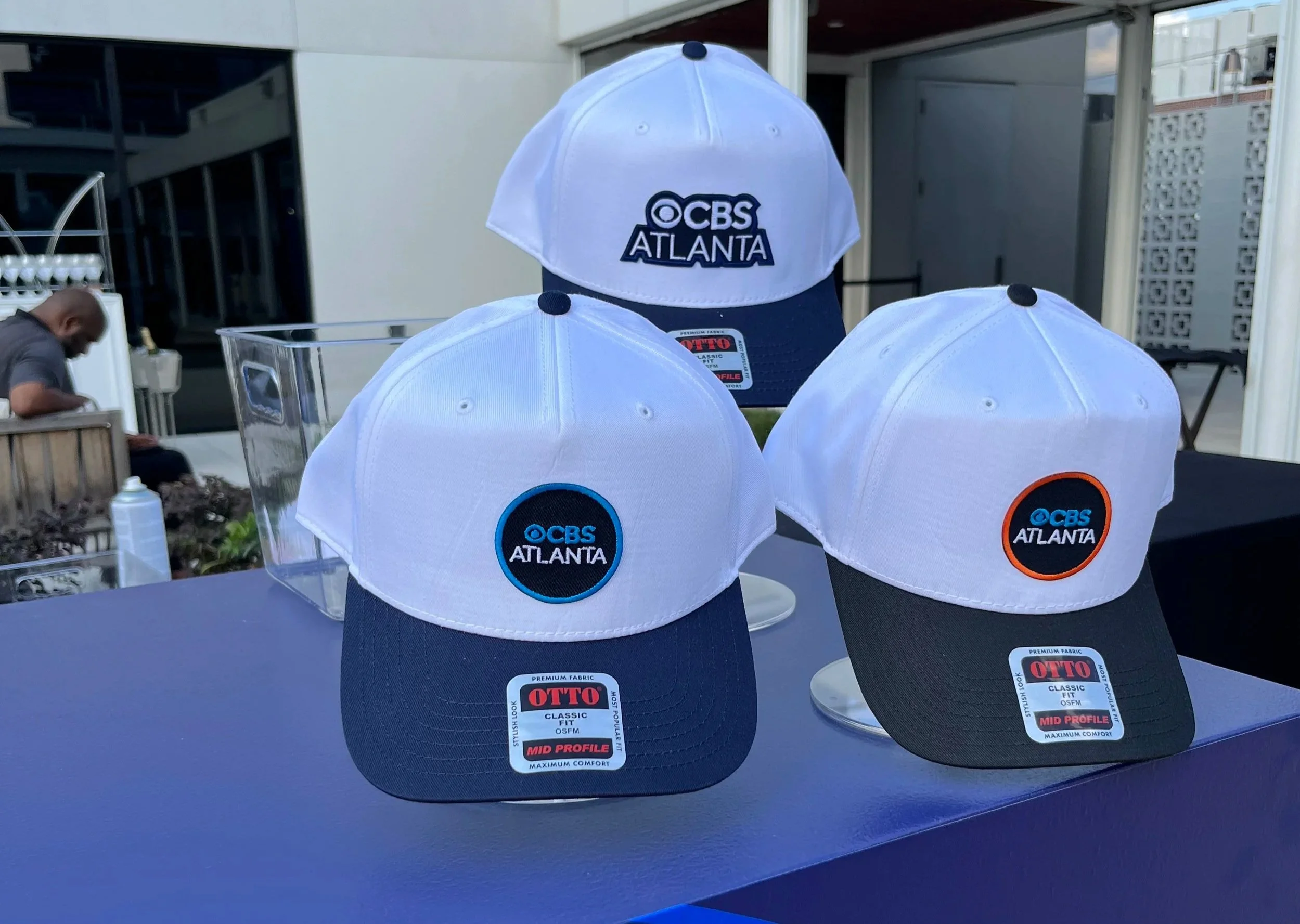 Three custom trucker hats featuring embroidered CBS Atlanta patches on display.