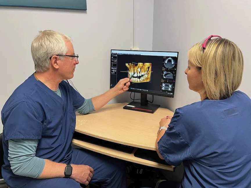 A dentist and a dental assistant discussing a 3D dental scan on a computer screen in a dental office.