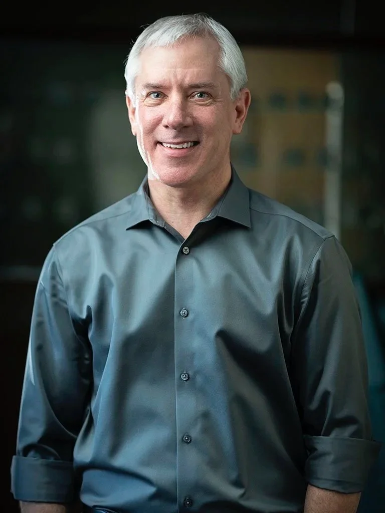 Headshot of a Dr. Kuhlberg with short white hair, wearing a gray button-down shirt, smiling at the camera.
