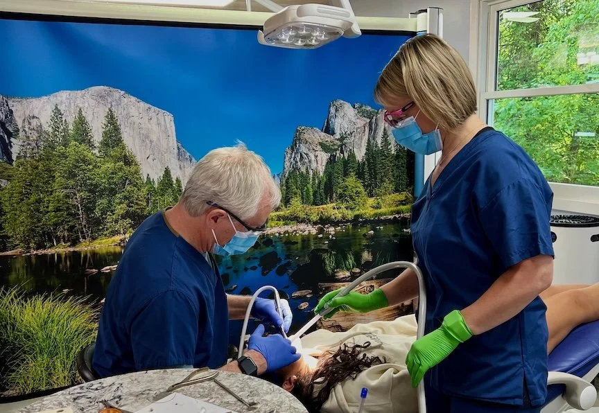 Medical professionals performing a procedure on a patient in a hospital room with a mountain landscape mural in the background.