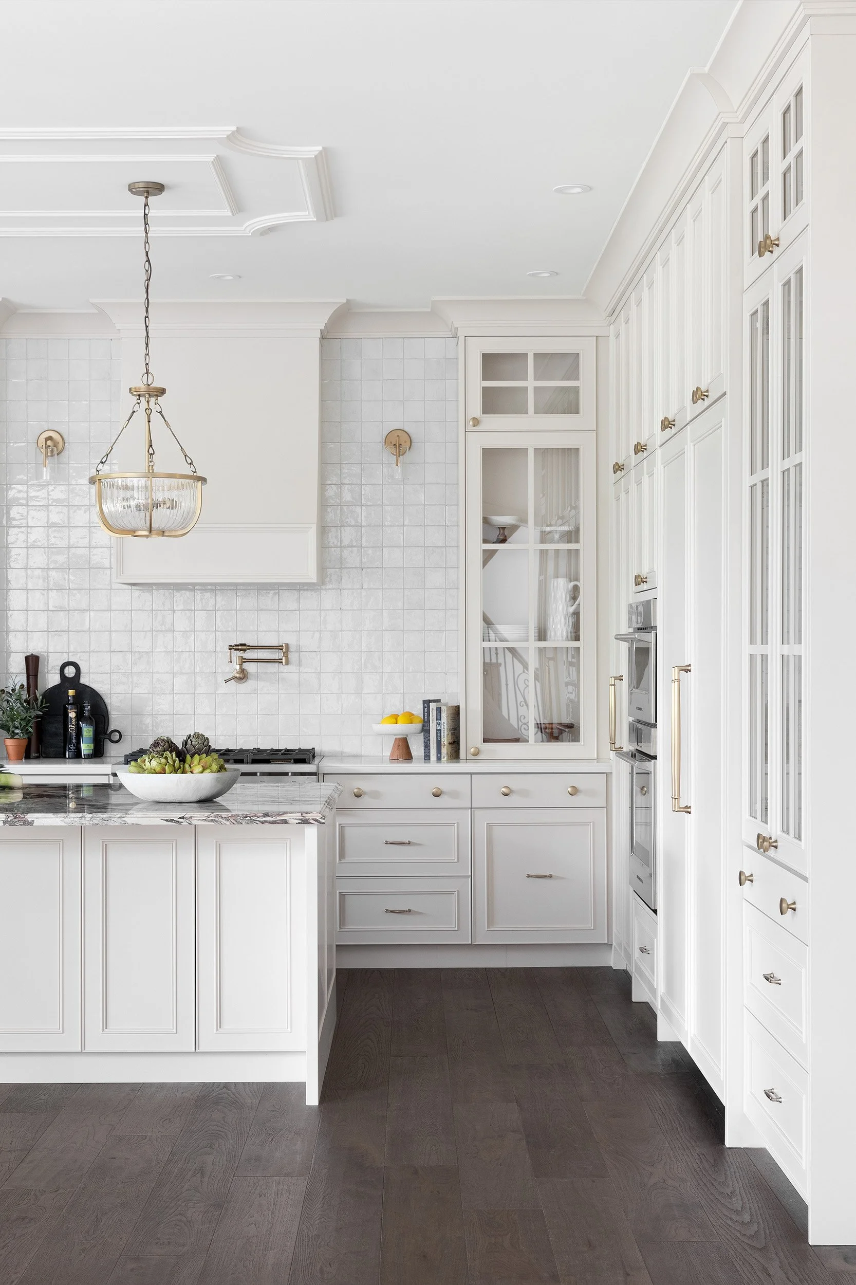 Transitional kitchen with white cabinetry, a marble island, dark hardwood floors, and a brass lighting.