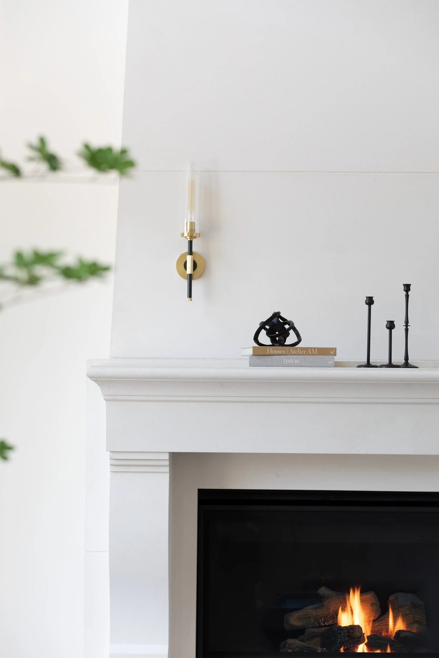 Close-up of a white plaster fireplace mantel with decorative items and a lit fireplace below.