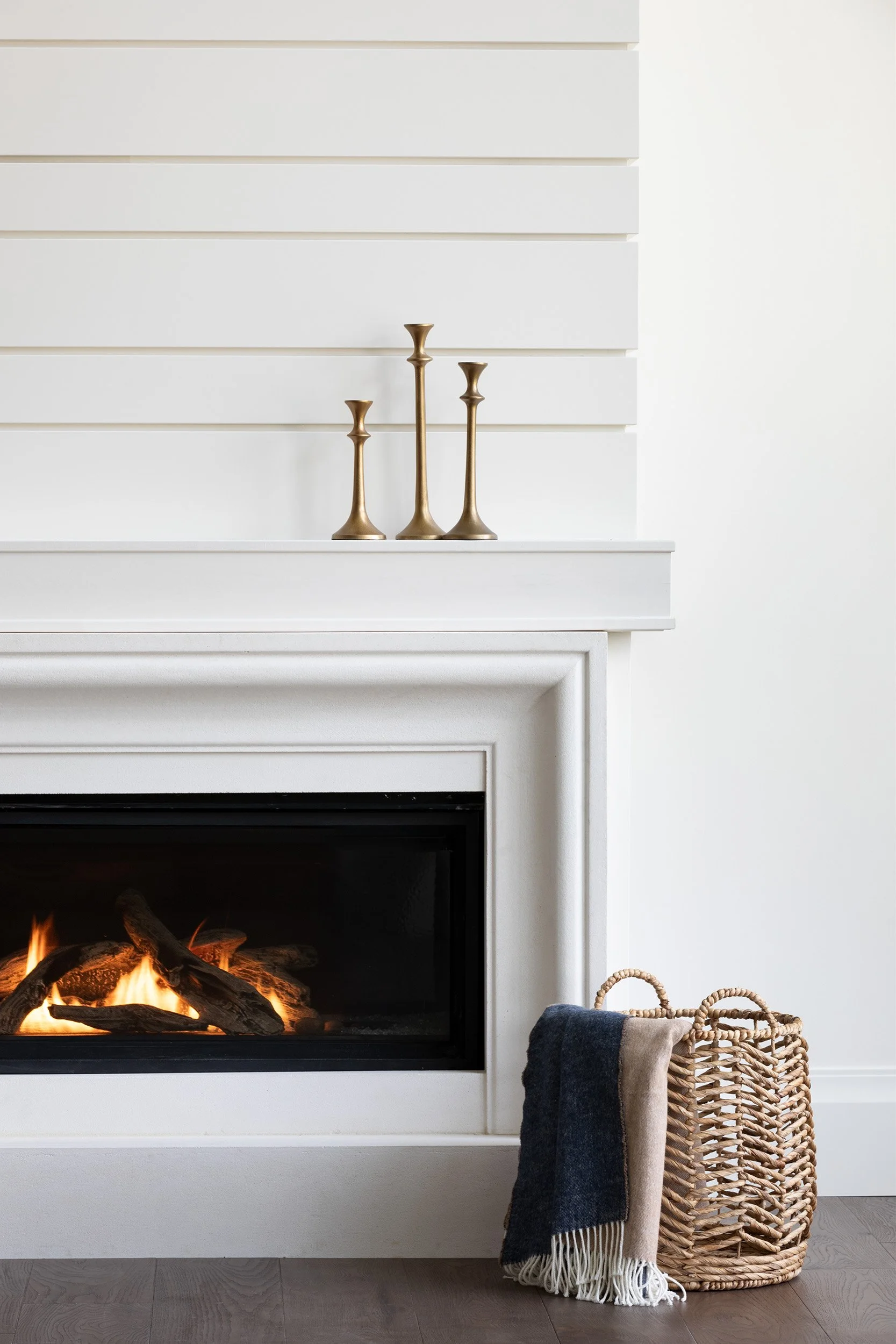 Living room with a plaster fireplace, three brass candlesticks on the mantle, a wicker basket with a blanket inside it.