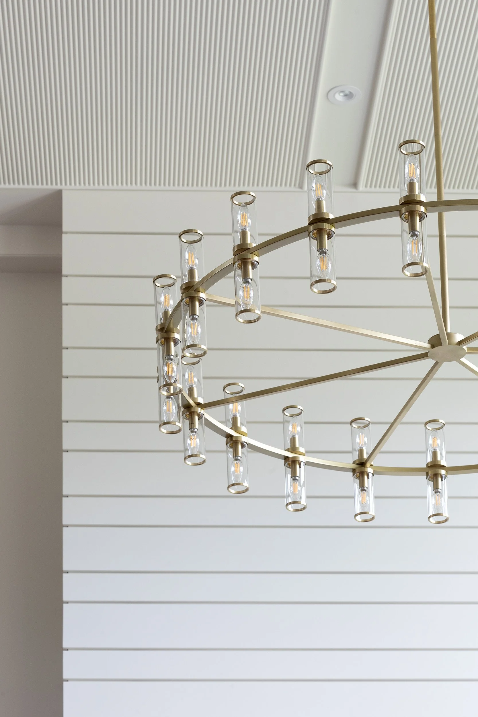 Close-up of a modern chandelier with multiple glass tube lights against a white paneled wall and ceiling.