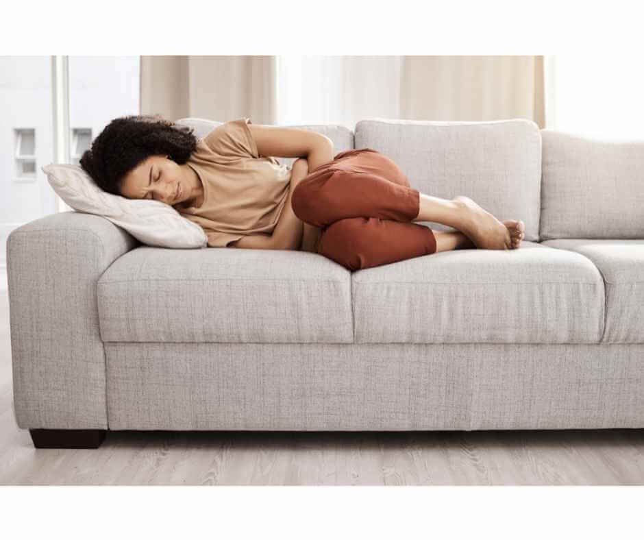Person resting on a couch with abdominal pain and fatigue, representing chronic symptoms of inflammatory bowel disease.
