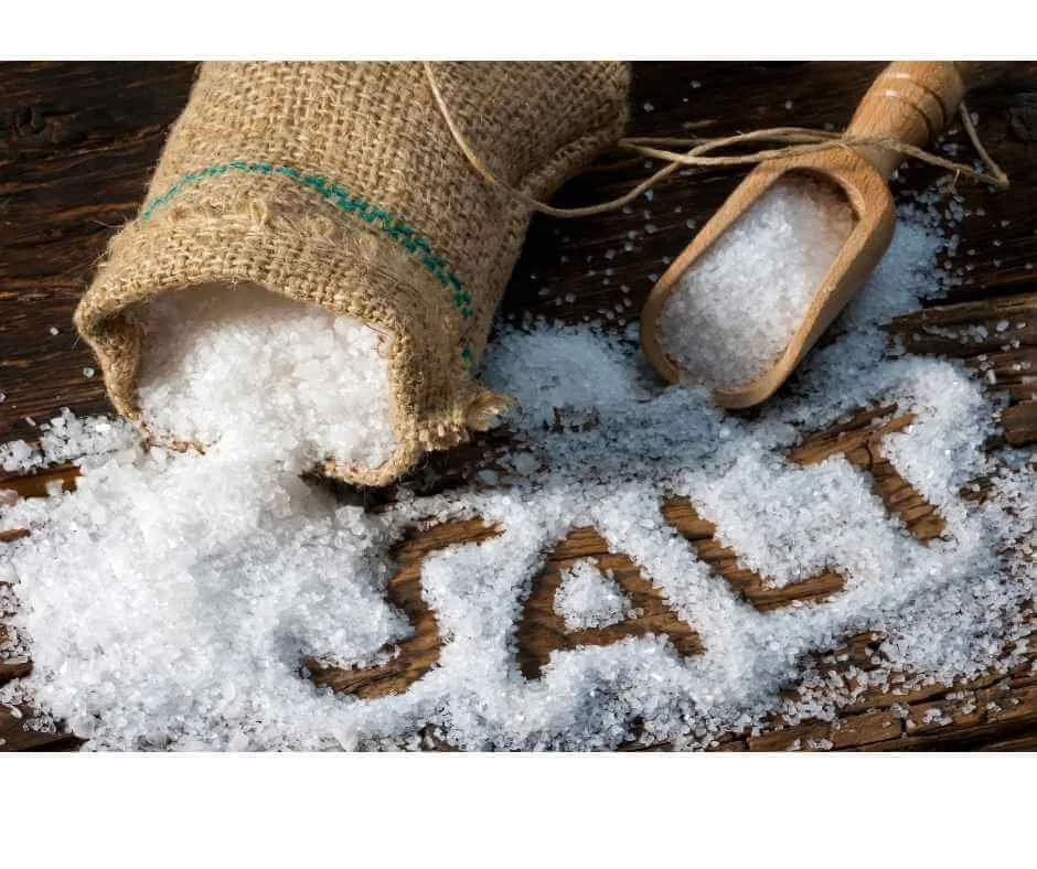 Coarse mineral sea salt spilled from burlap sack with wooden scoop, illustrating sodium balance and blood pressure health