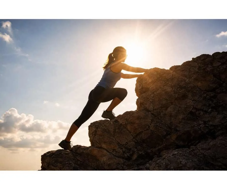 Midlife woman climbing a rocky mountain at sunset, symbolizing metabolic resilience, cellular energy, and healthy aging.