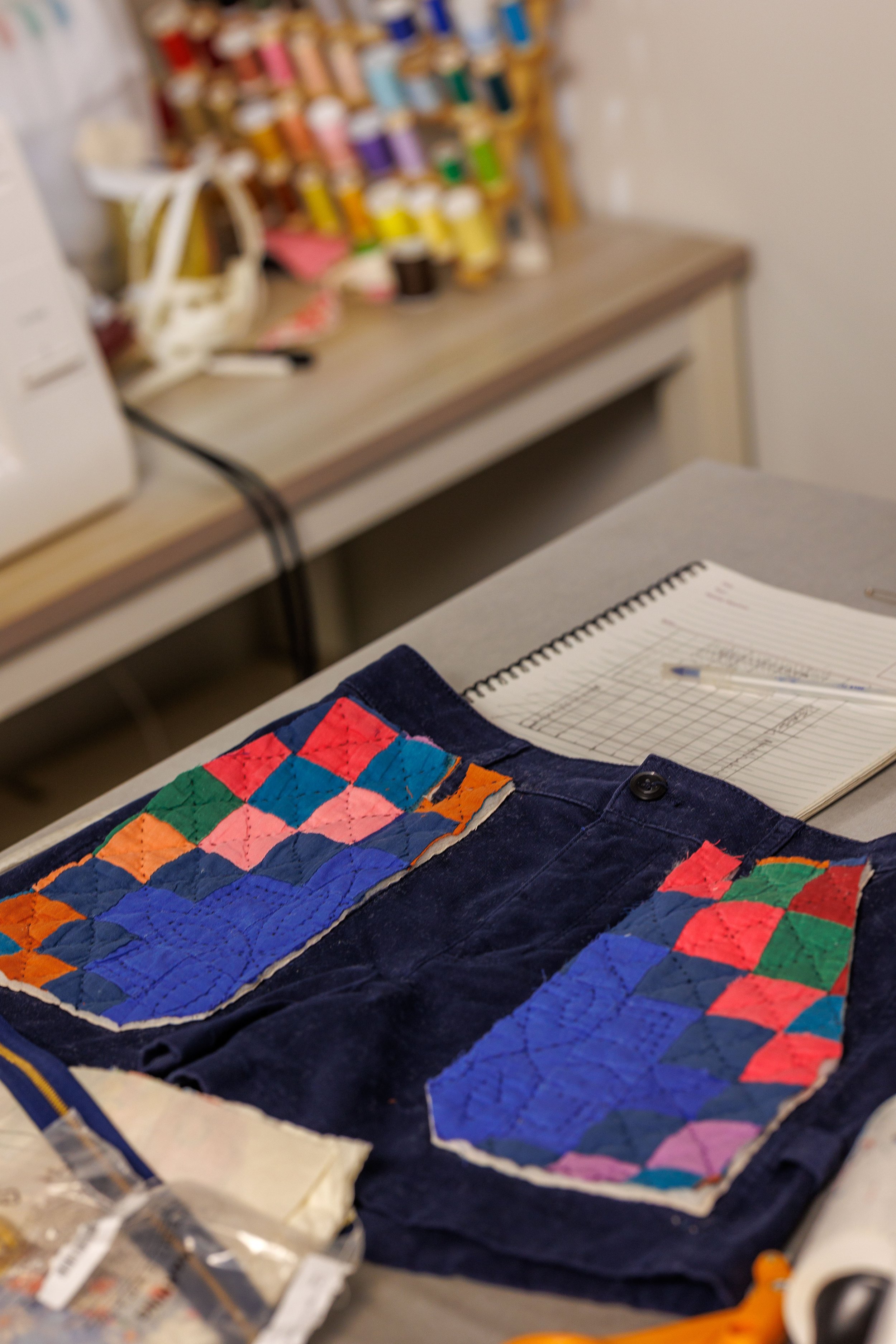 A quilting project featuring a colorful patchwork quilt laid out on a table, with sewing supplies and instructions nearby. The background shows a collection of spools of thread.