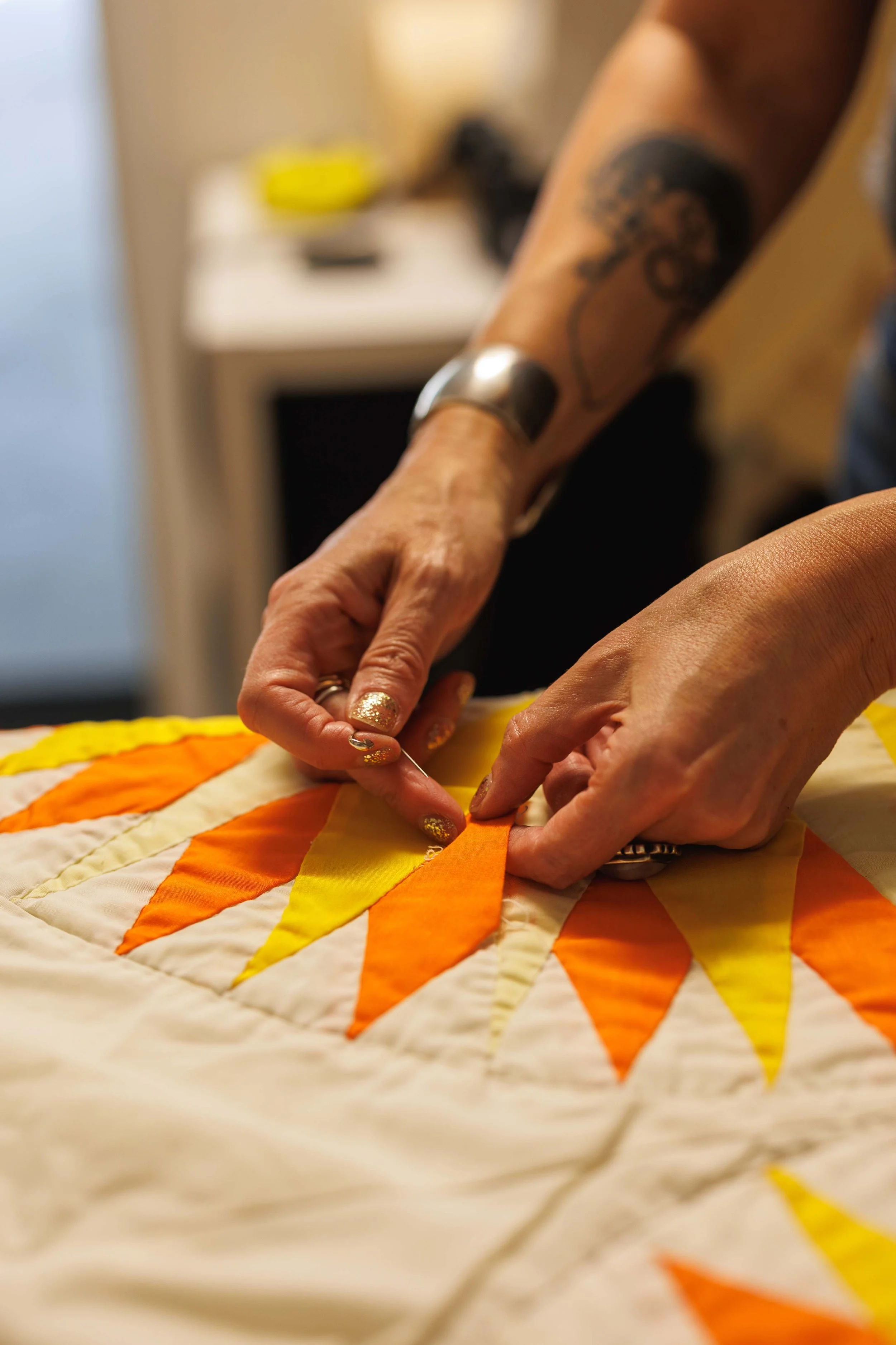 Close-up of a person's hands sewing a colorful quilt with orange and yellow triangles.