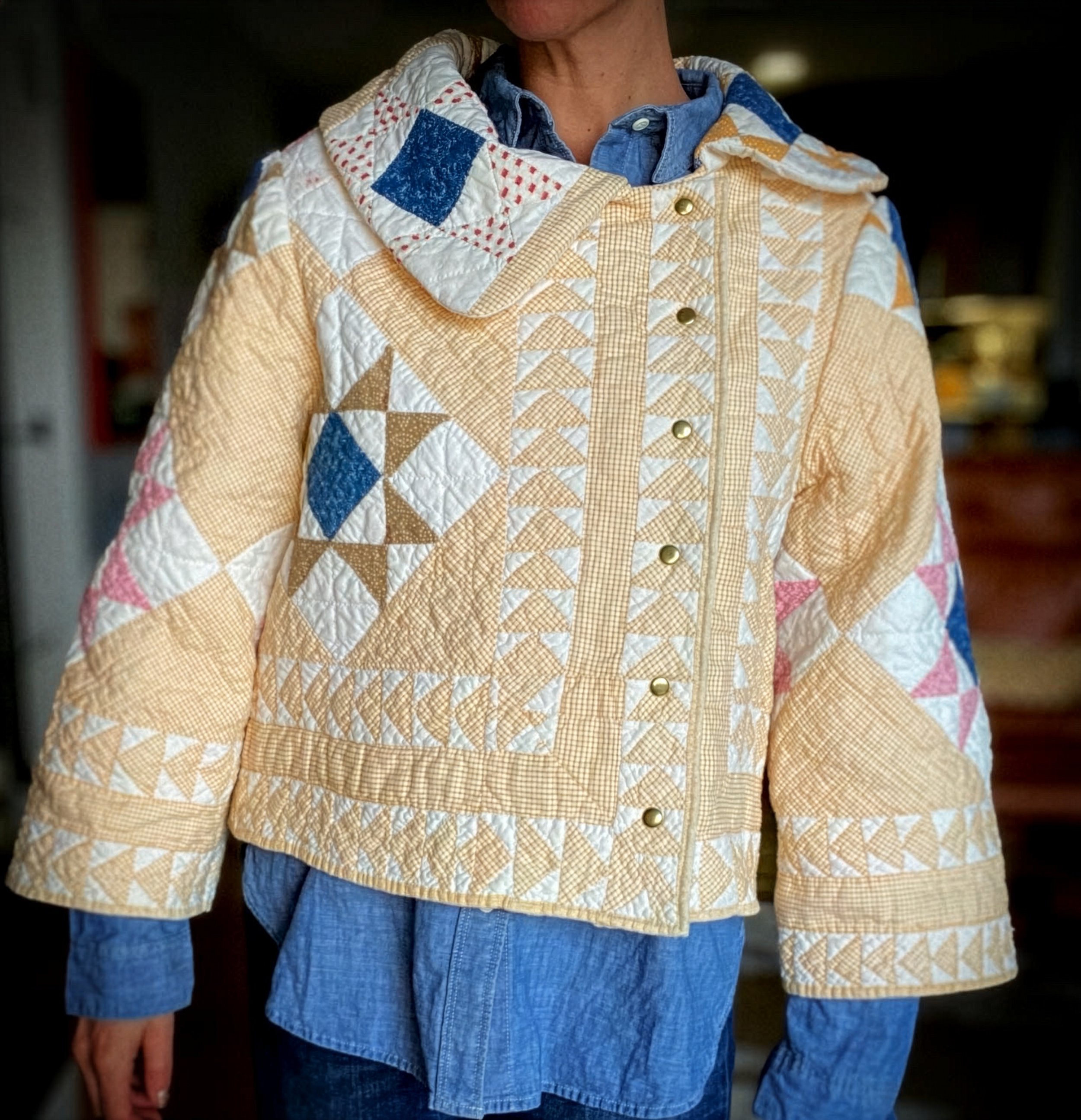 Person wearing a denim shirt under a patchwork quilted jacket with geometric patterns and buttons.