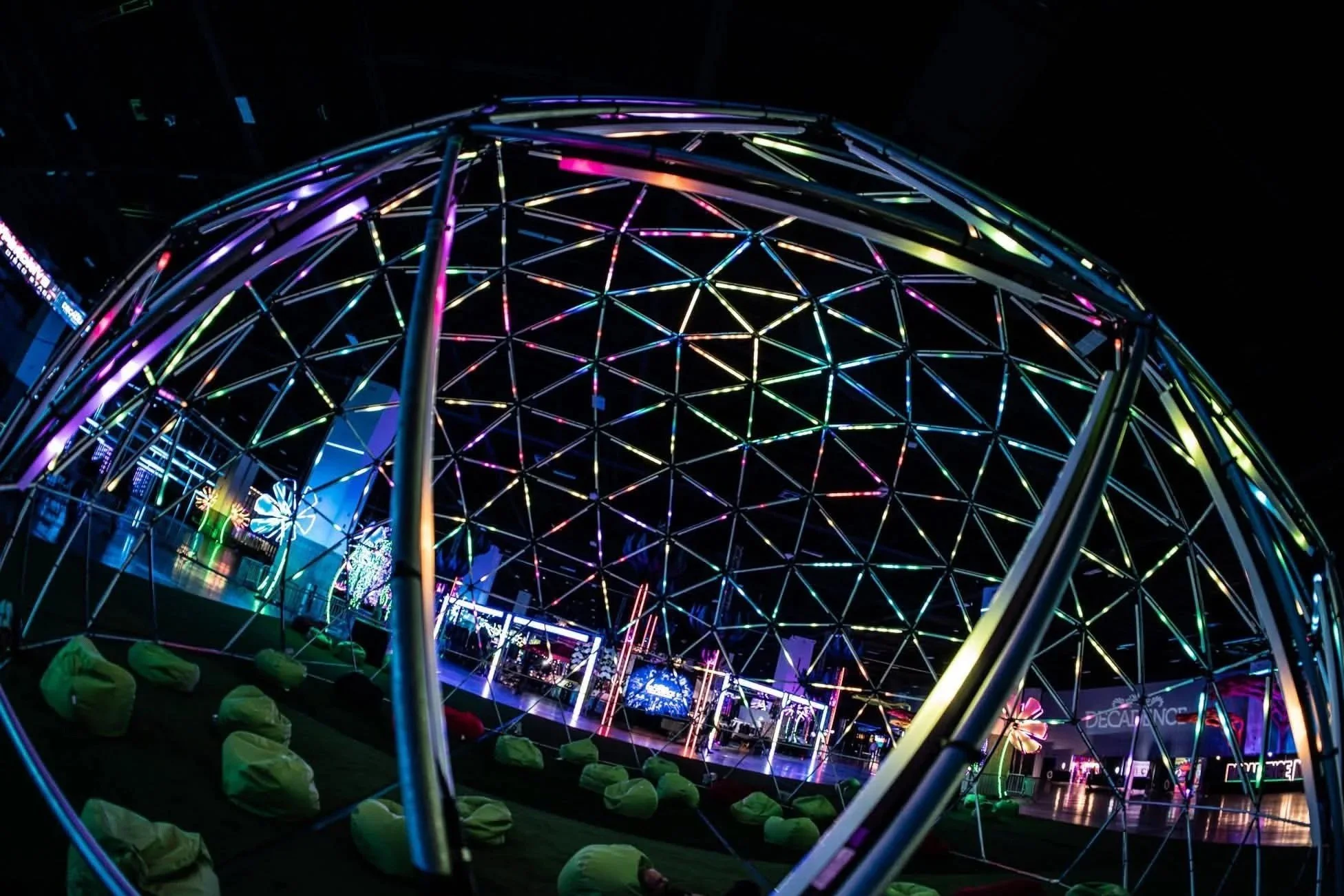 A colorful LED-lit dome structure at night with bean bag chairs underneath.