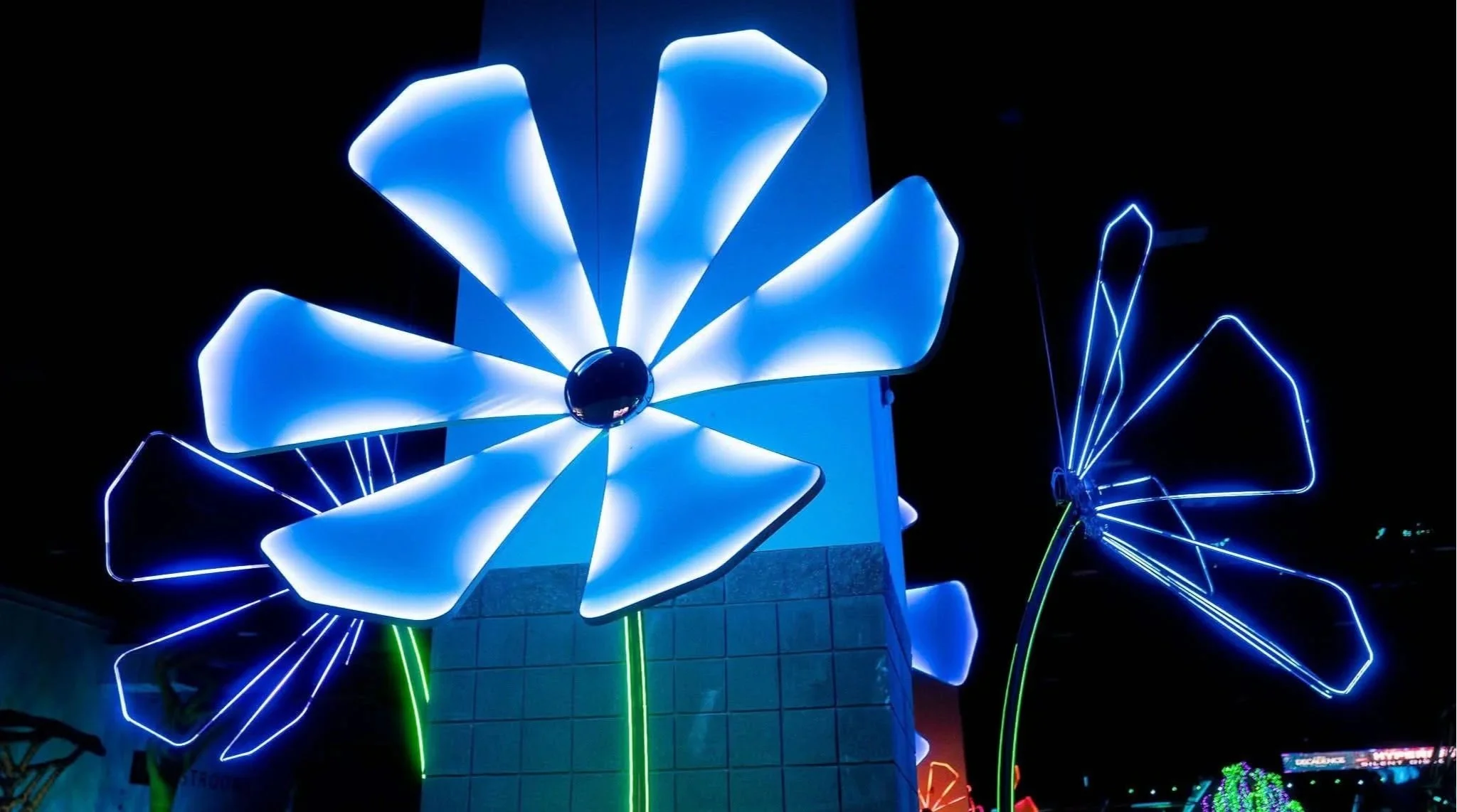 Neon blue and green illuminated flower sculptures at night in a music festival.