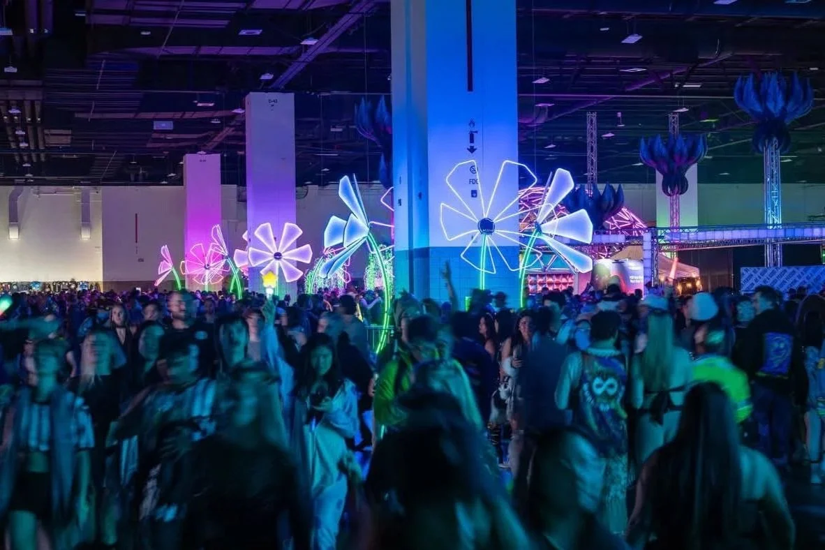 Crowd of people at an indoor event with colorful illuminated giant flower decorations.