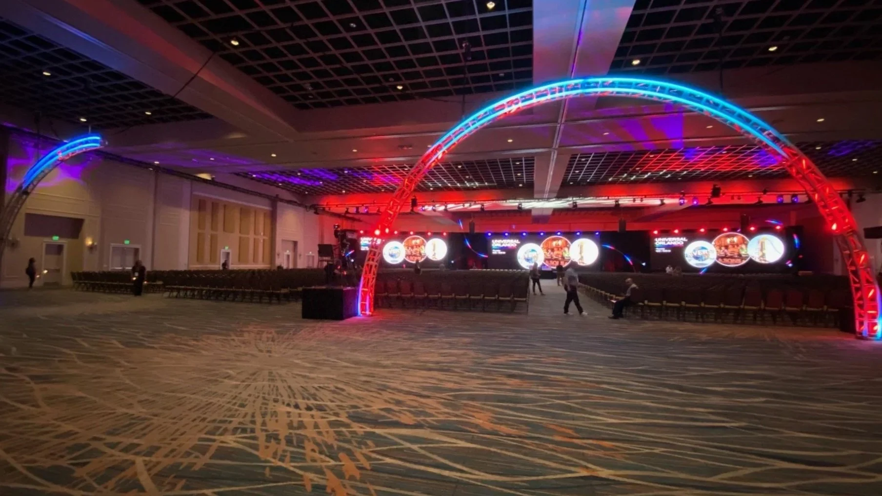 Conference room setup with colorful LED lighting and empty chairs, featuring a large screen and LED illuminated arches, Electronic Sales and Production, Denver, CO.