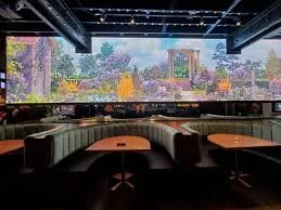 Interior of a 'Wonderyard' restaurant or bar with curved booth seating and wooden tables, featuring a large LED wall displaying a colorful garden scene. The space is dimly lit with a contemporary design. Electronic Sales and Production, Denver, CO.