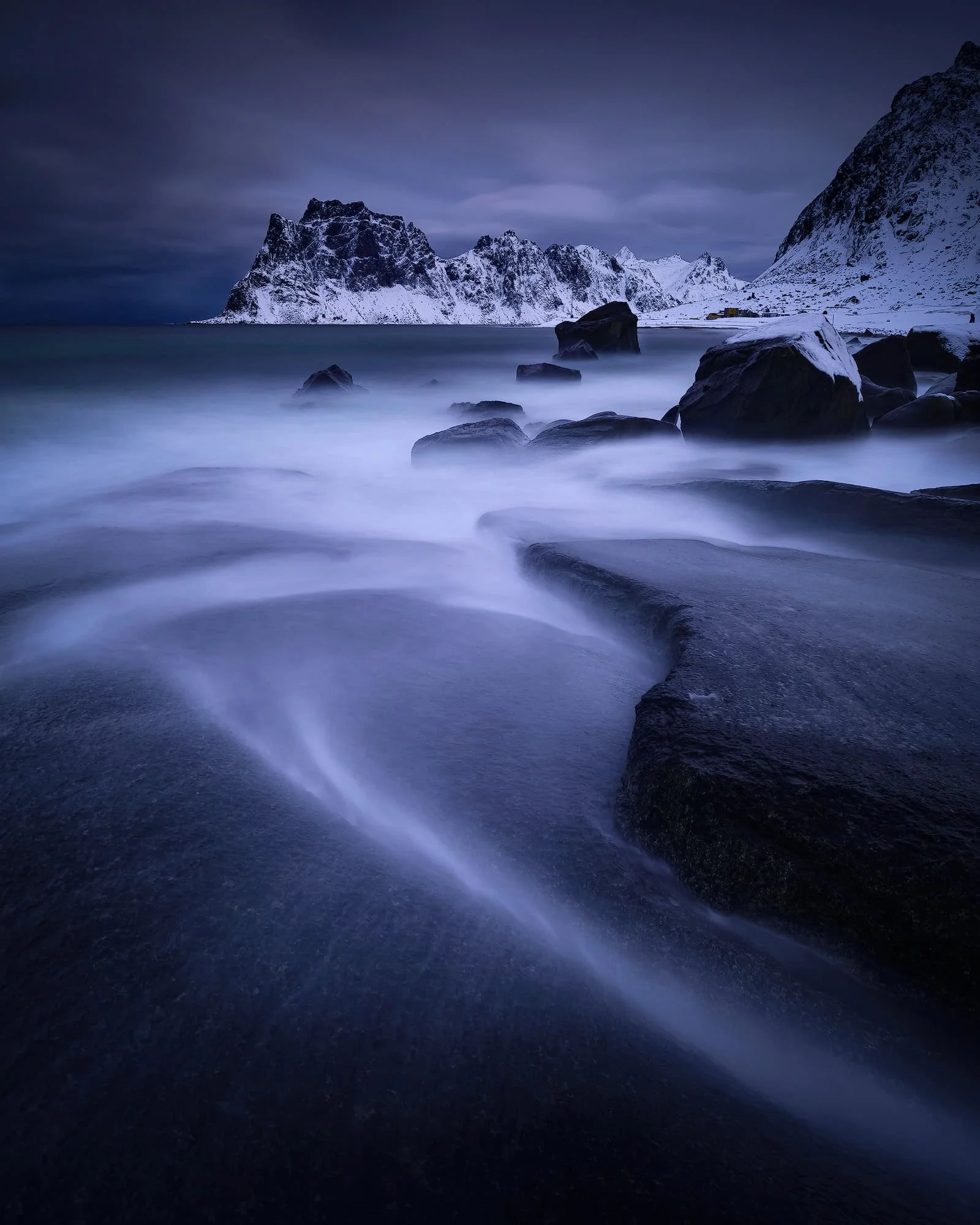 Blue-hour Lofoten beach with misted water pulled into soft lines over dark rock