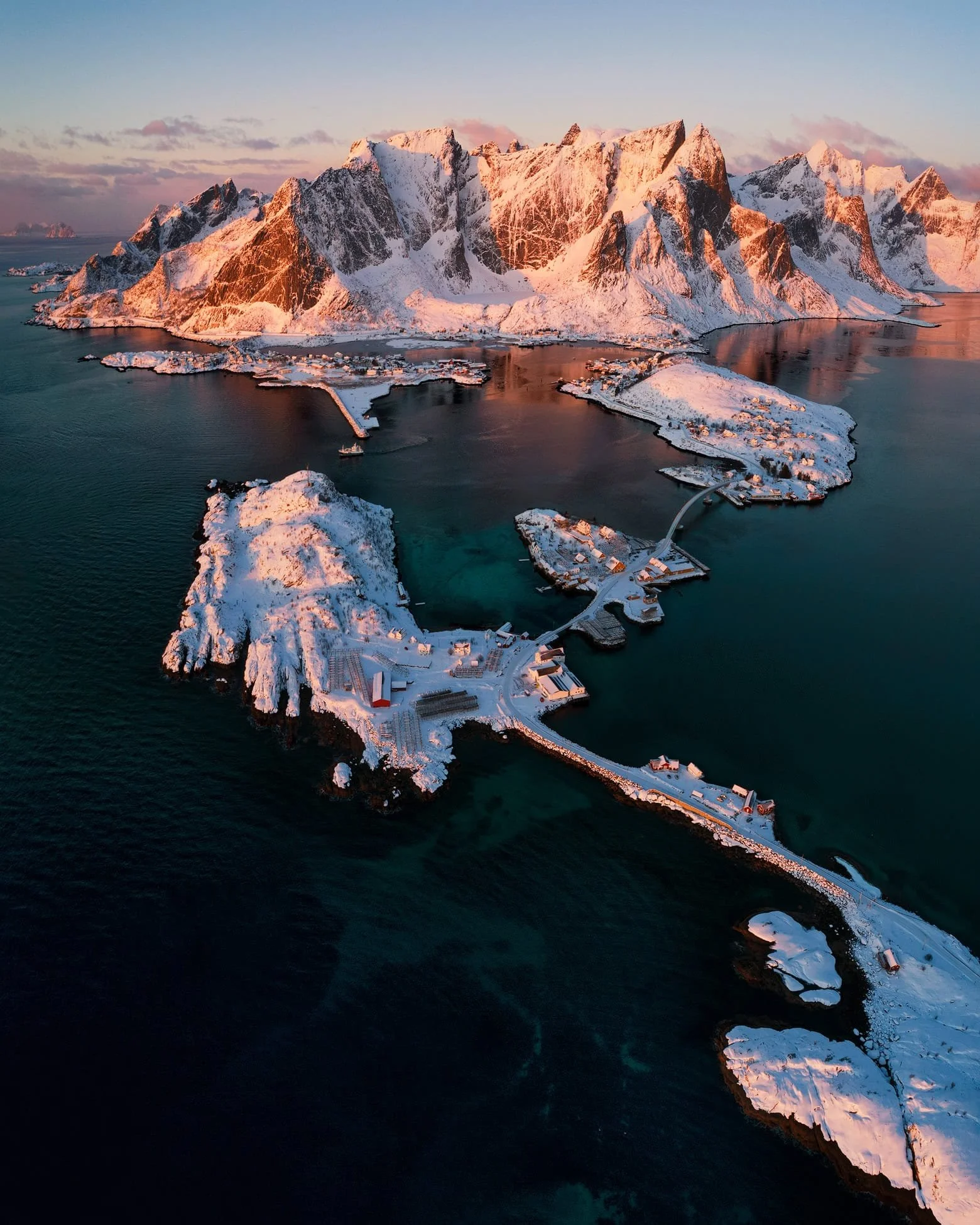 Aerial view of the yellow cabins against cool winter mountains at Sakrisøy, Lofoten, Norway with Reine in the background