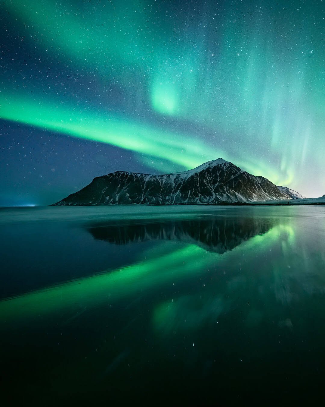 The Aurora Borealis reflecting in the wet sand of the gorgeous Skagsanden beach, one of the best locations for northern lights photography at Lofoten Islands, Norway