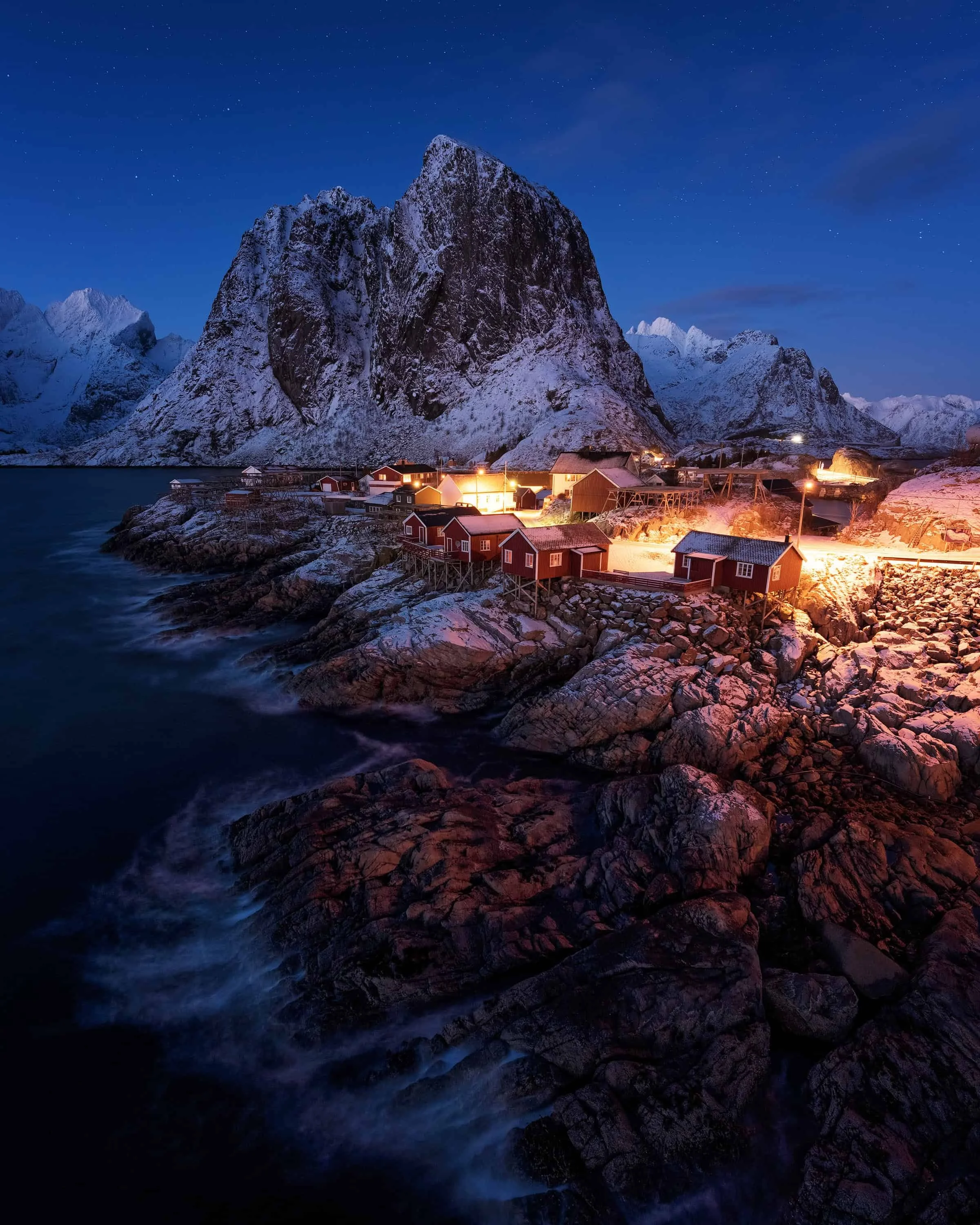 Classic view of red rorbuer cabins and towering peaks at Hamnøy in winter blue hour, Lofoten, Norway