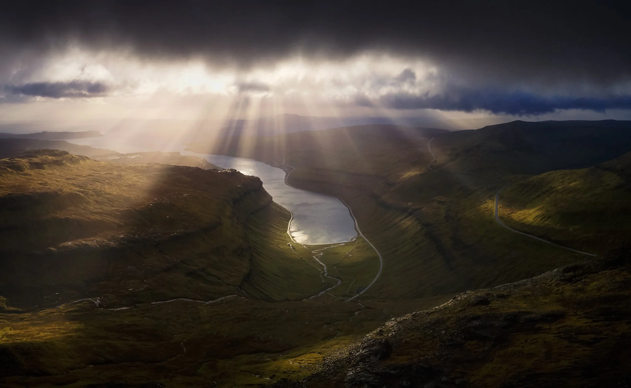 God rays breaking through storm clouds over a fjord valley after rain, Faroe Islands