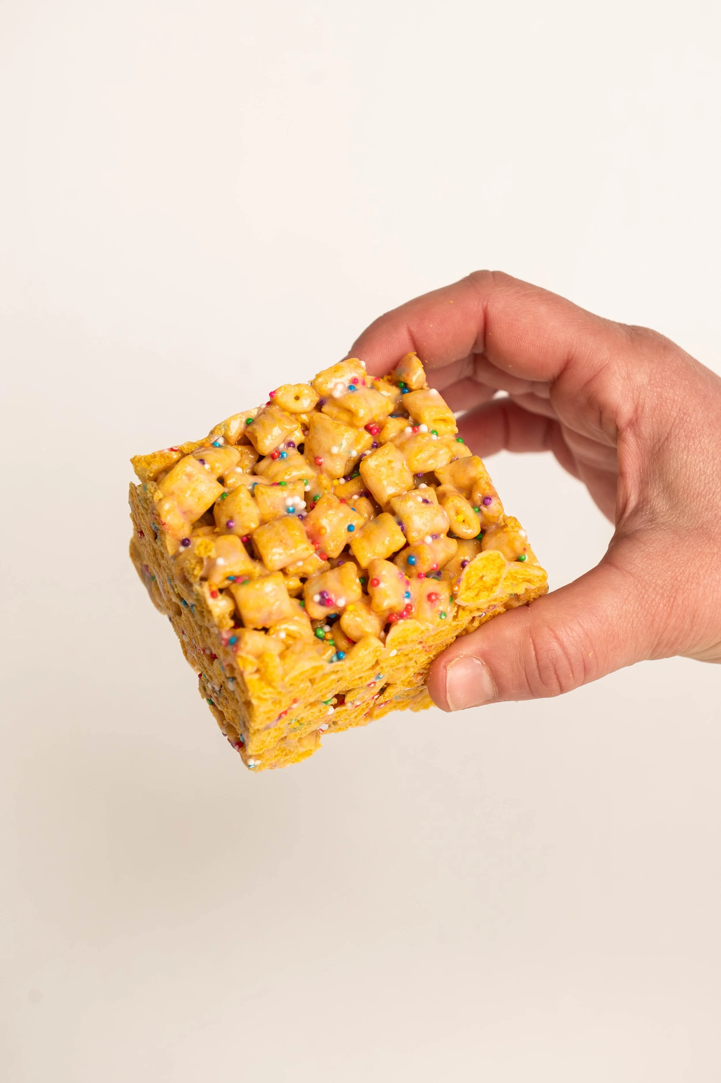 Hand holding a Rice Krispies treat topped with caramel, mini M&Ms, and colorful sprinkles.