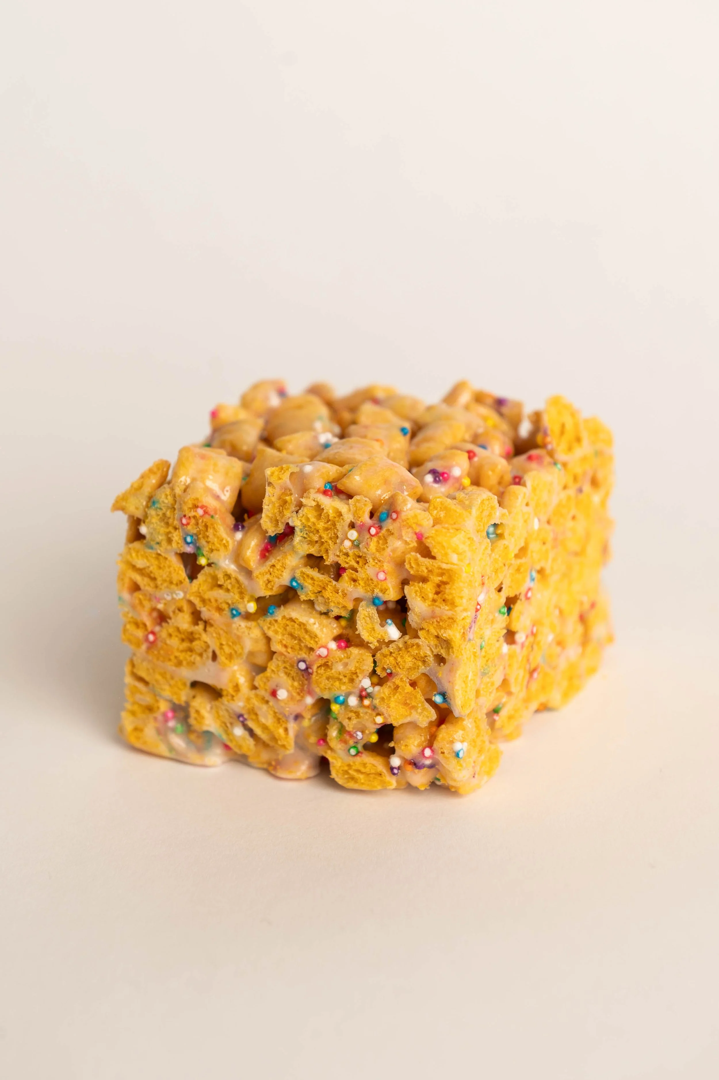 A close-up of a rice crispy treat with colorful sprinkles and frosting.