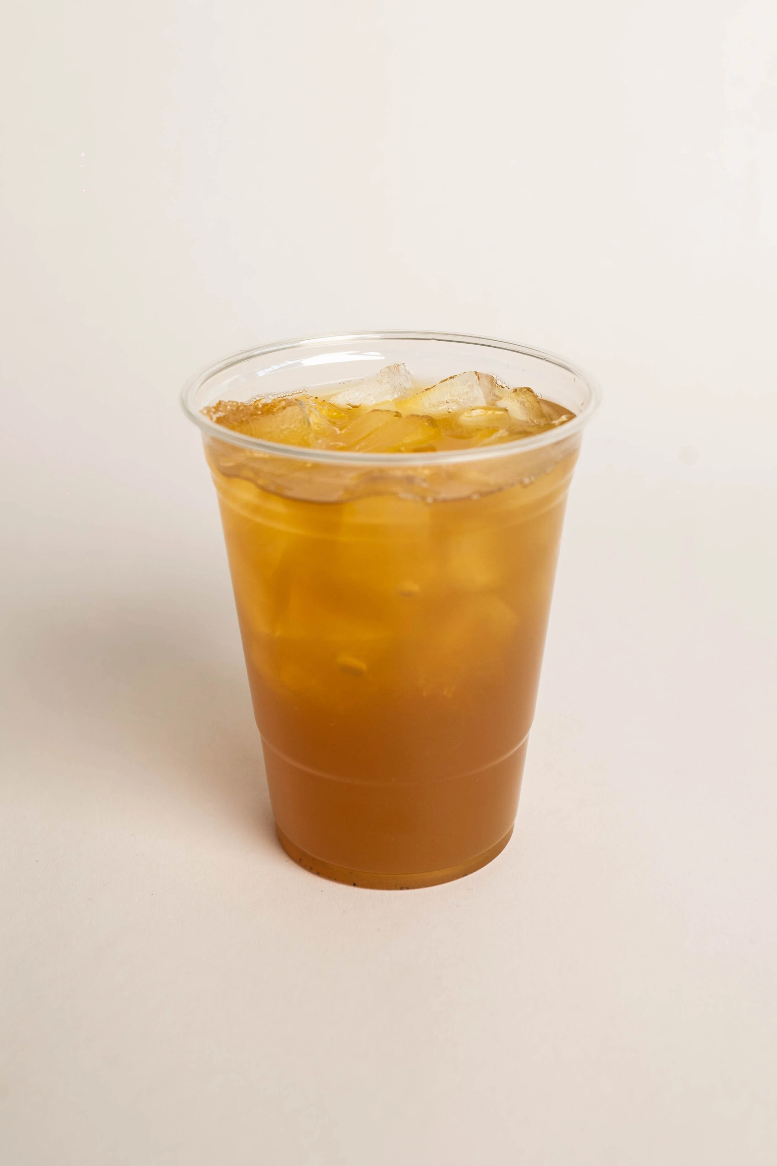 A clear plastic cup filled with iced tea and ice cubes, placed on a plain white surface.