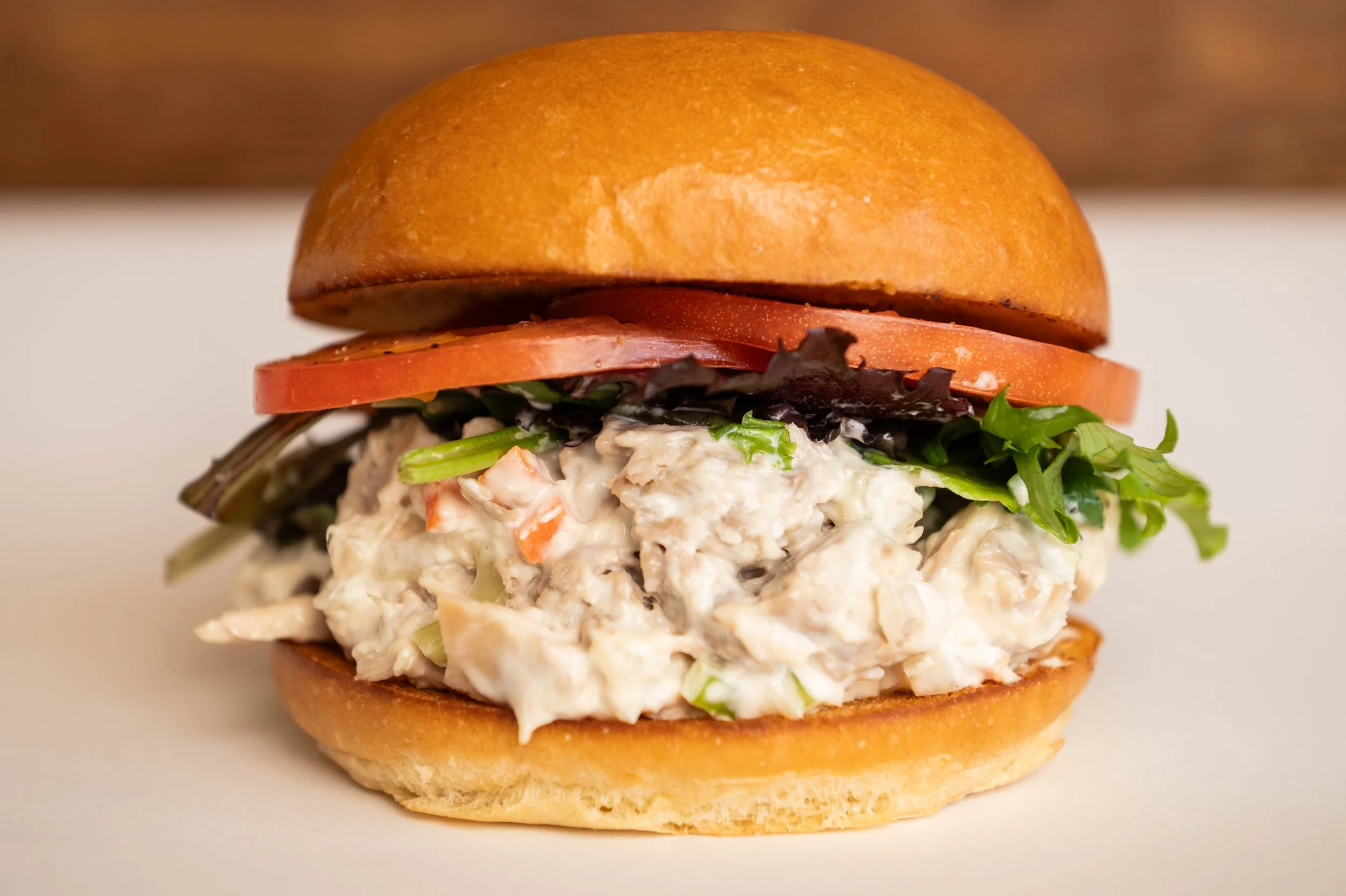 Close-up of a chicken salad sandwich with lettuce, tomato, and bun.