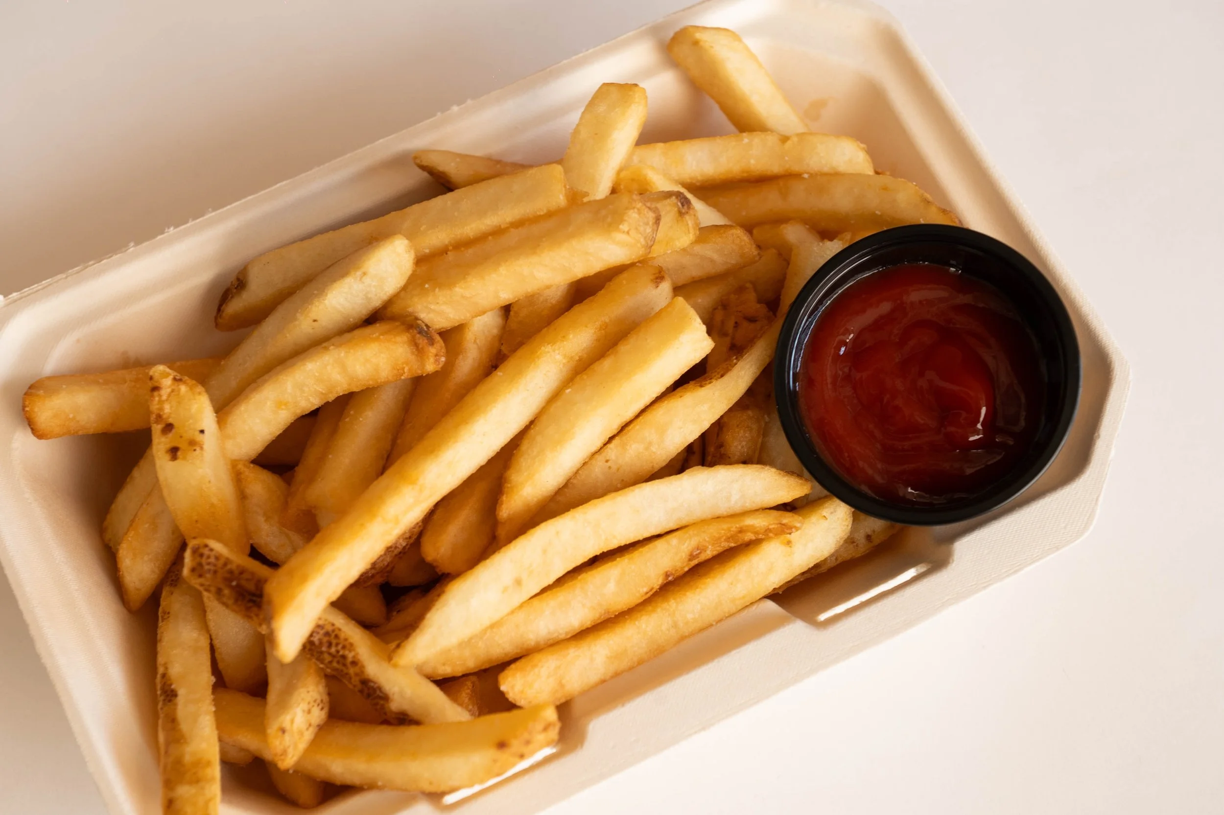 French fries with a side of ketchup in a small black cup in a white takeout container