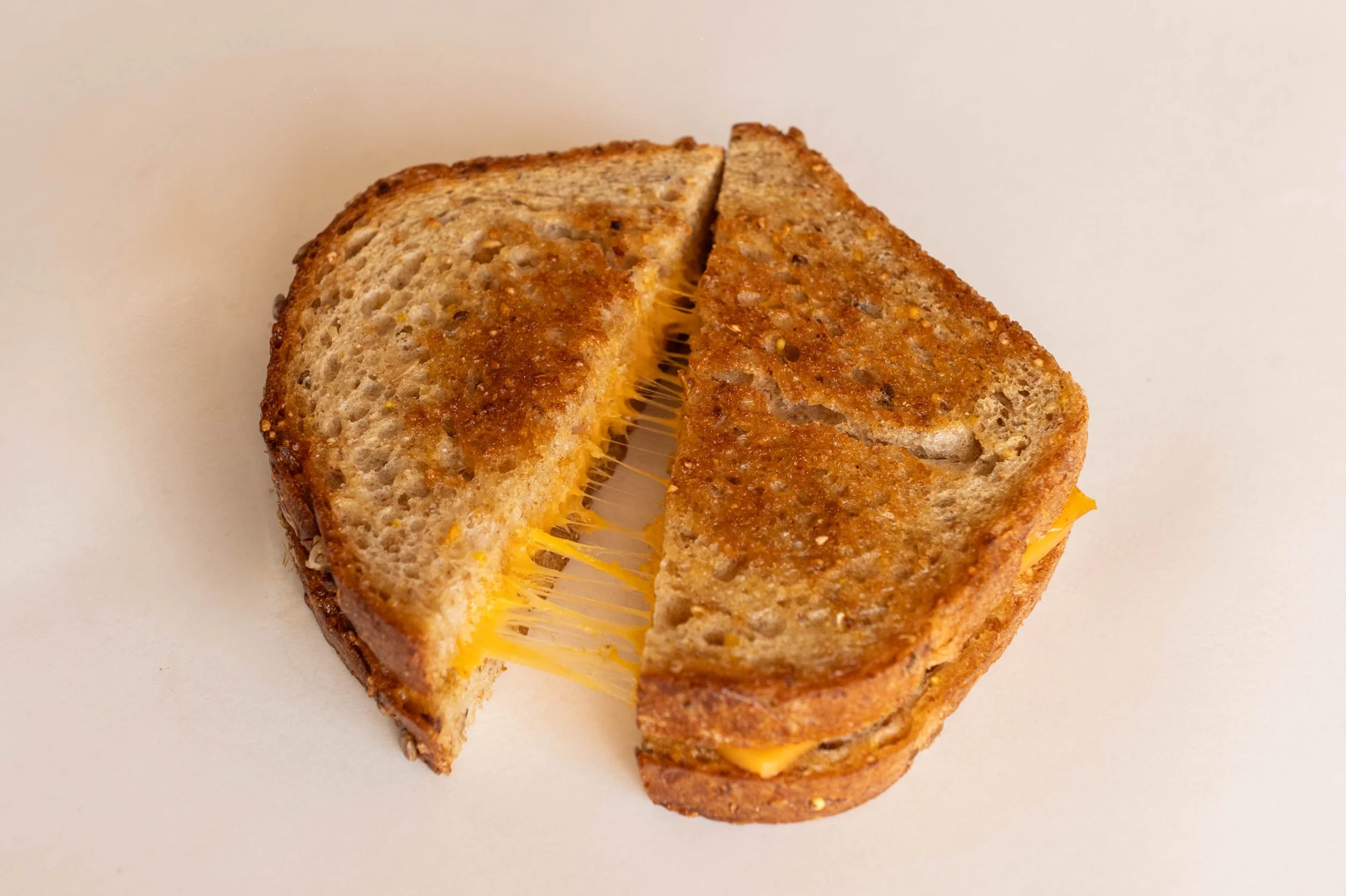 Close-up of a grilled cheese sandwich cut in half on white background, showing melted cheese inside.