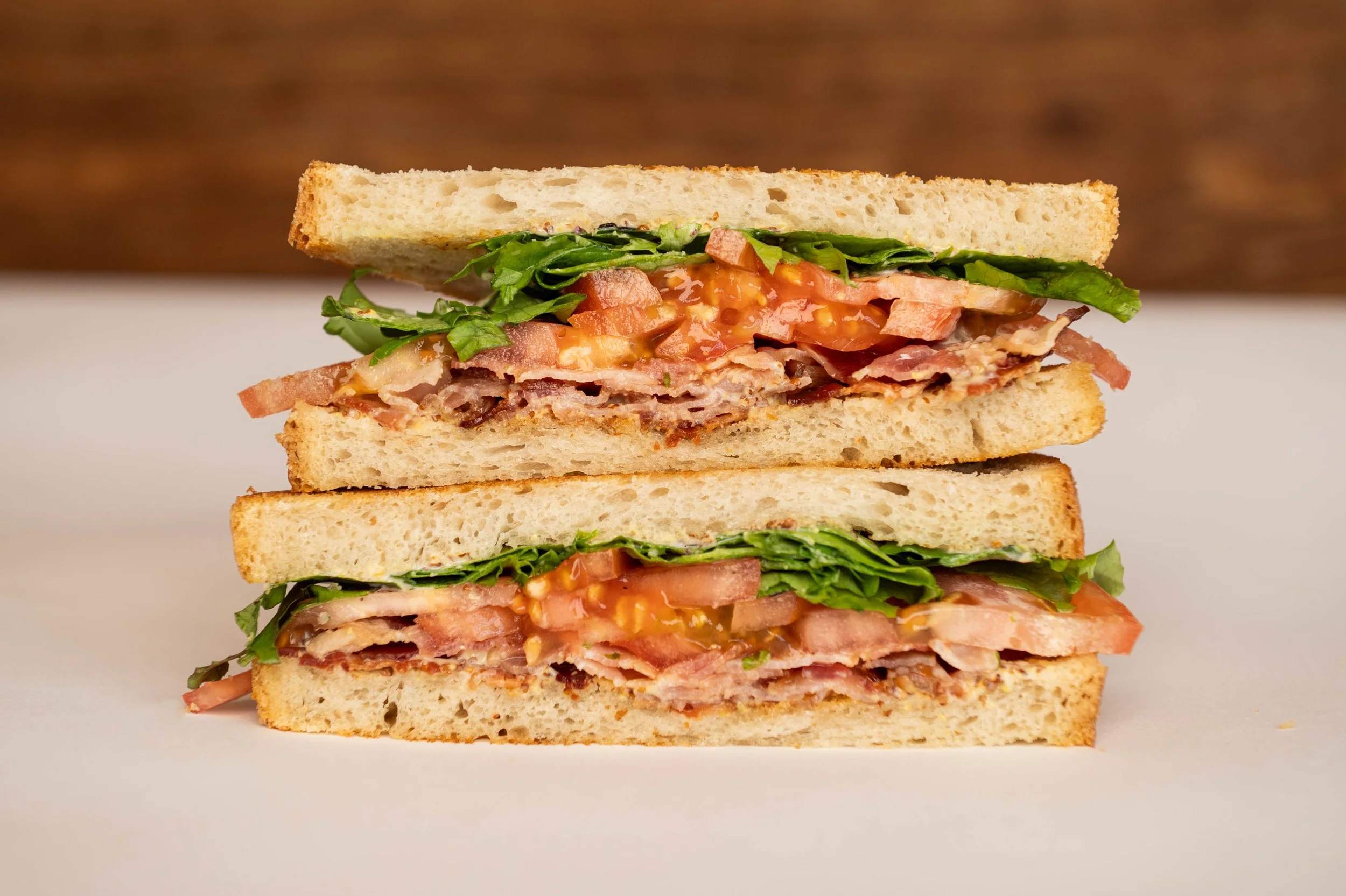Two halves of a BLT sandwich stacked with bacon, lettuce, tomato, and bread.
