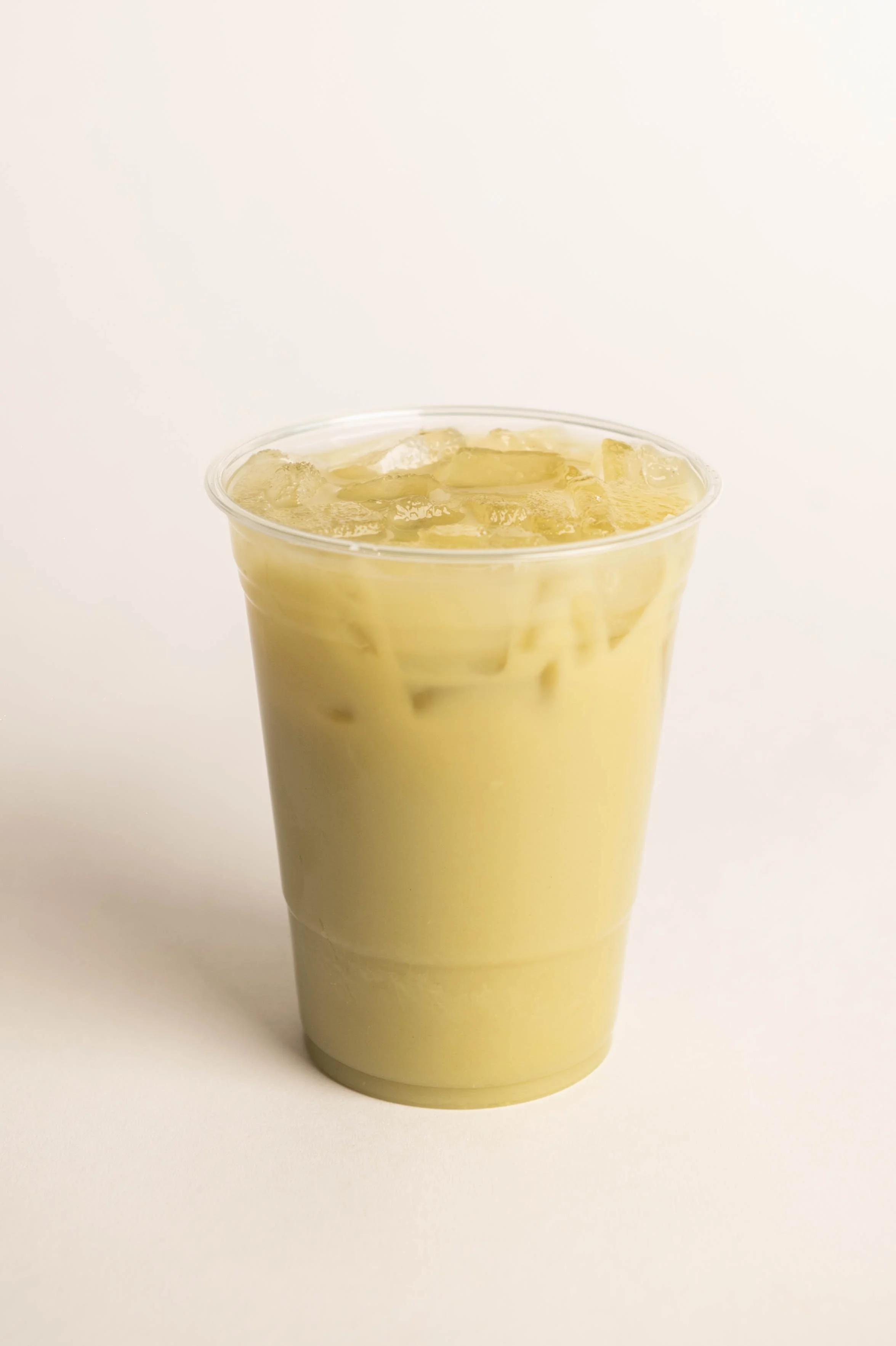 A clear plastic cup filled with iced matcha latte with ice cubes on top.
