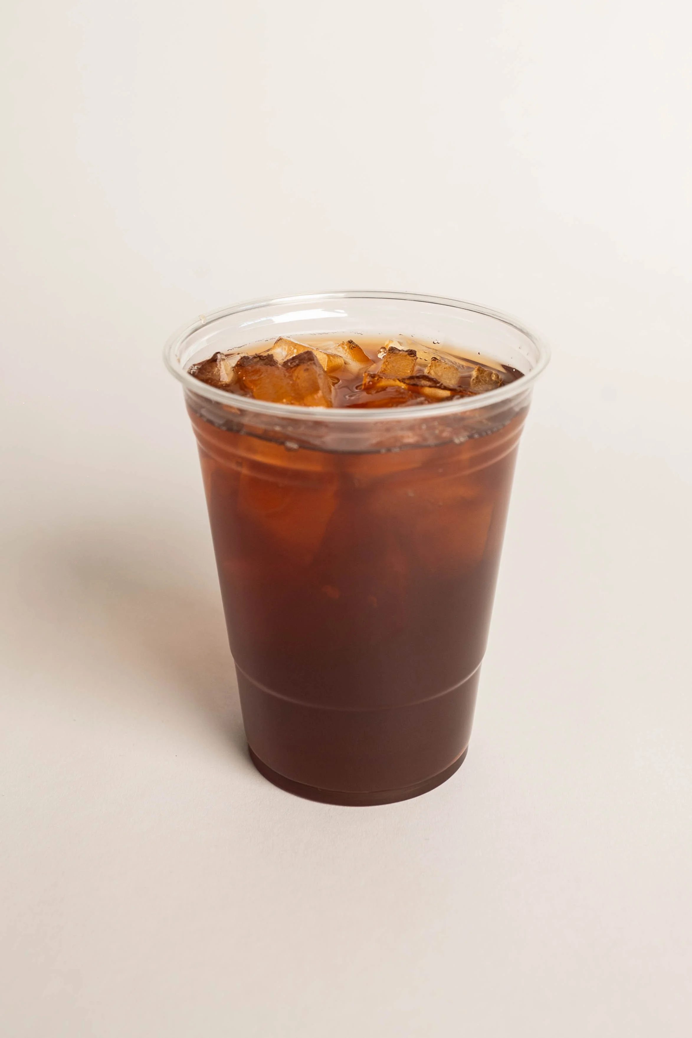 A clear plastic cup filled with iced coffee and ice cubes on a plain white surface.